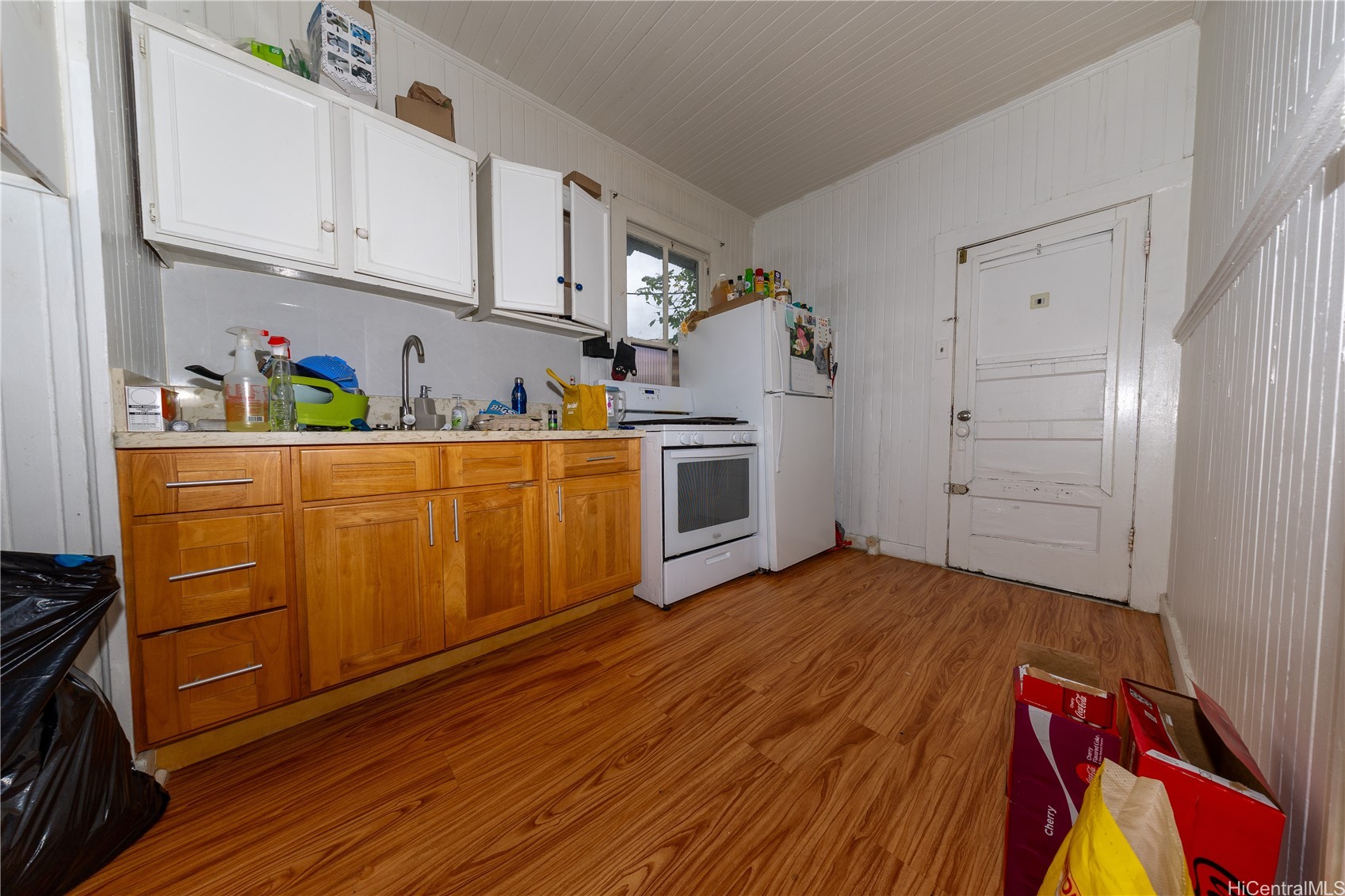 Kitchen with wood cabinets, white appliances, paneled walls, and wood-look flooring.