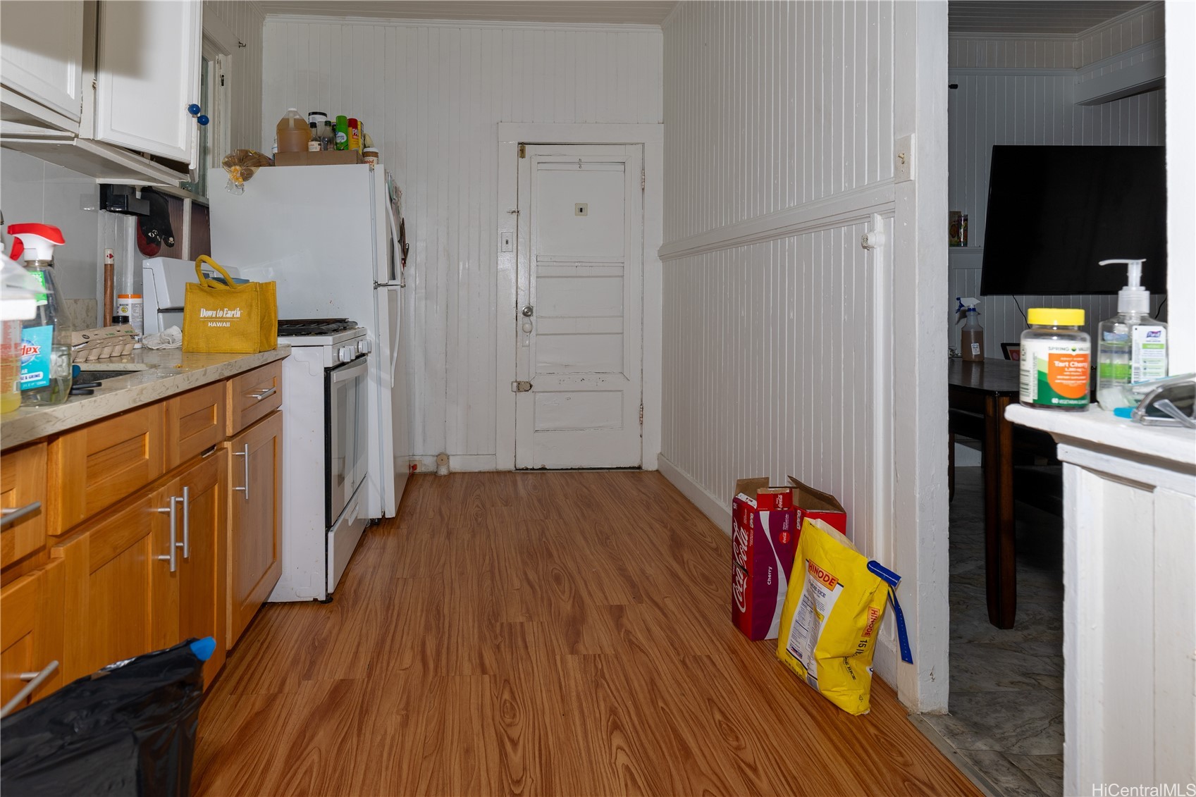 Narrow kitchen with wood cabinets, white appliances, wood-look flooring, and a paneled door.
