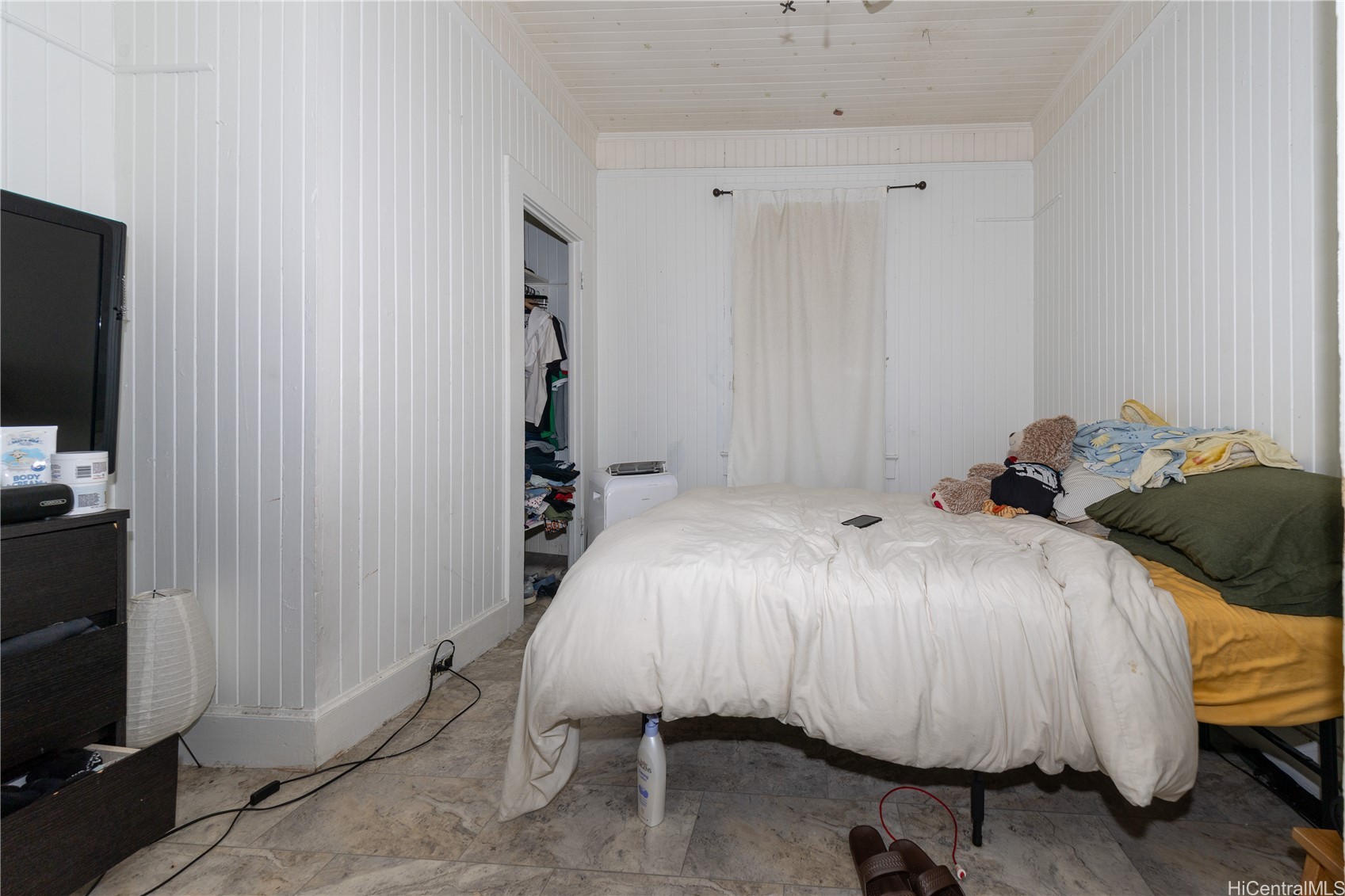 Bedroom with white paneled walls, two beds, and an open clothes closet.