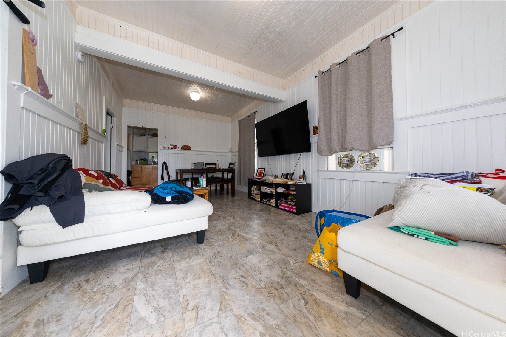 Living room with white sofas, paneled walls, tile floors, and a television.