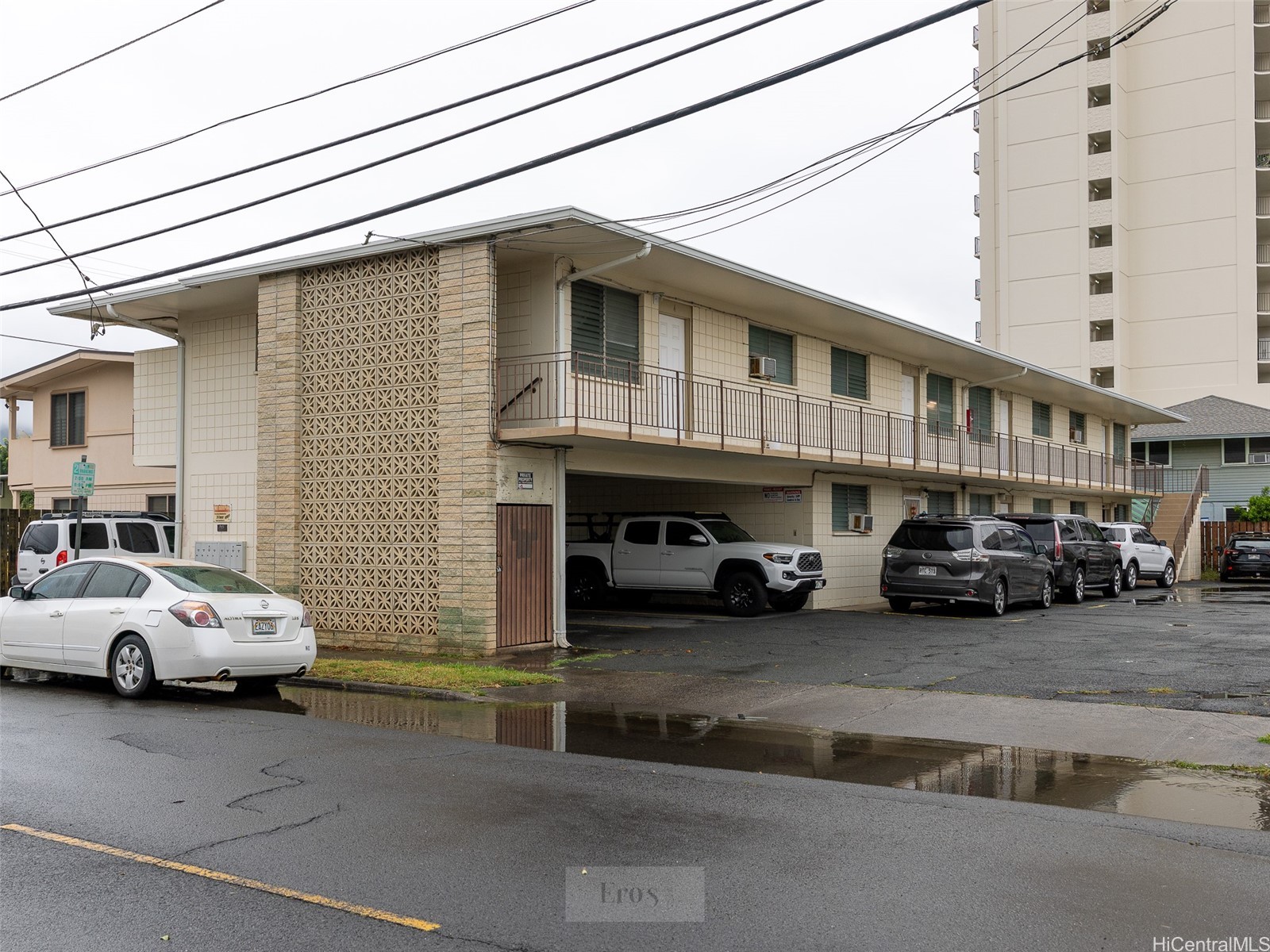 Two-story apartment building with an open-air walkway, patterned breeze-block facade, and covered parking.