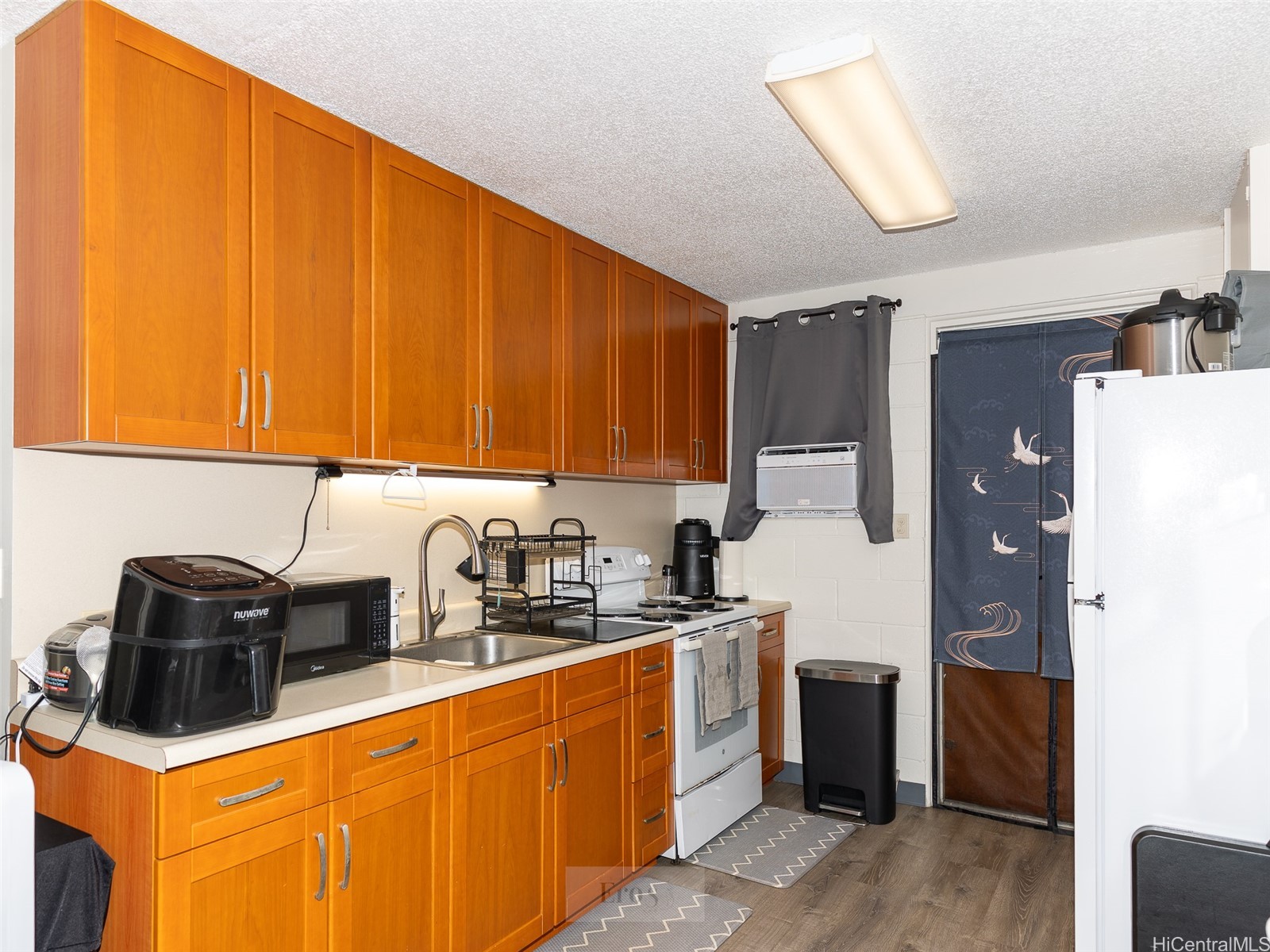 Kitchen with warm wood cabinets, a long countertop, and white appliances.
