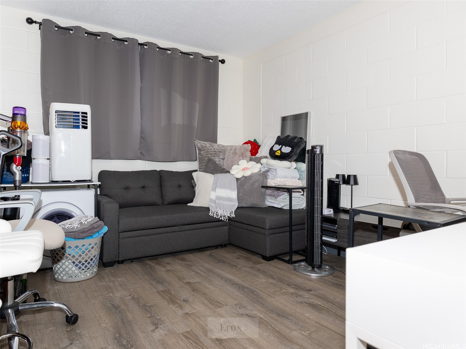 Furnished room with a gray sectional, laundry appliances, portable air conditioner, and desk.