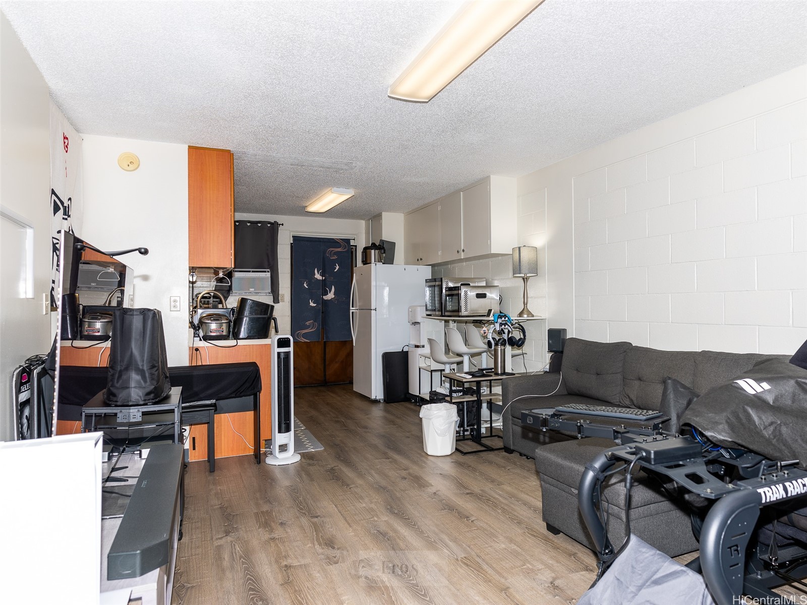 Furnished studio living area with a compact kitchenette, gray sectional sofa, and exercise equipment.