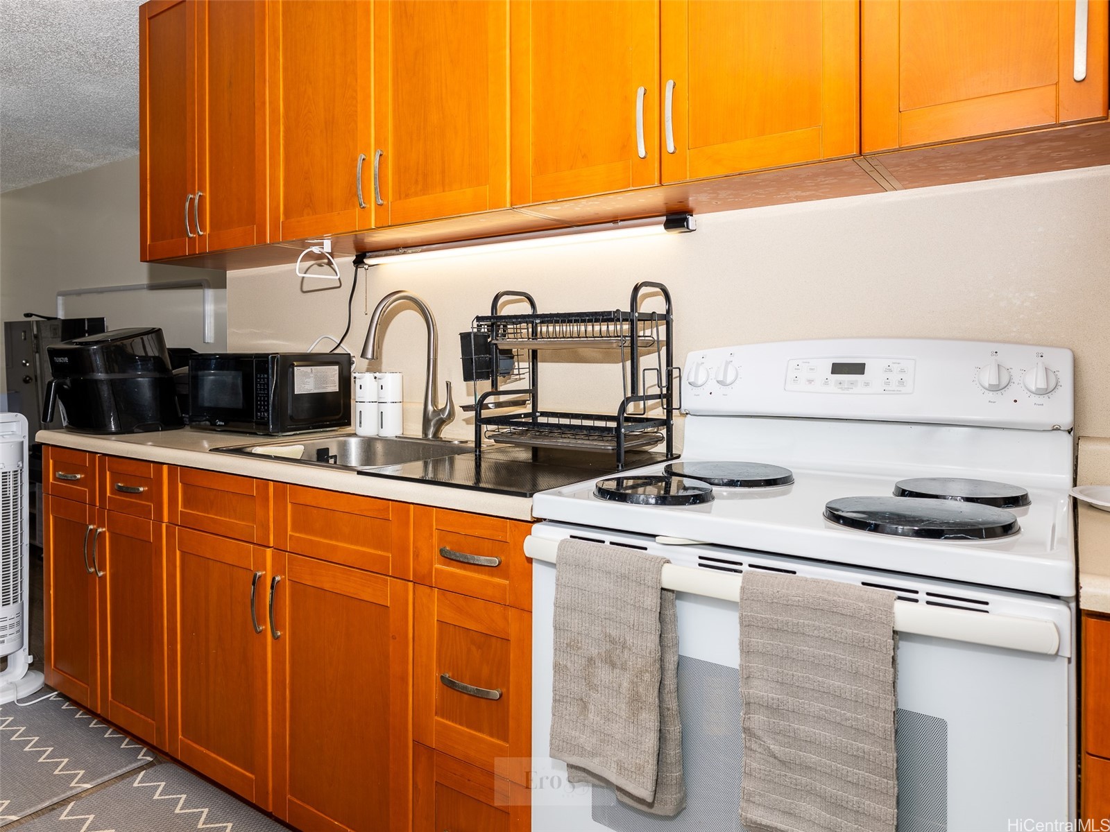 Kitchen with orange wood cabinets, white electric range, sink, and countertop appliances.