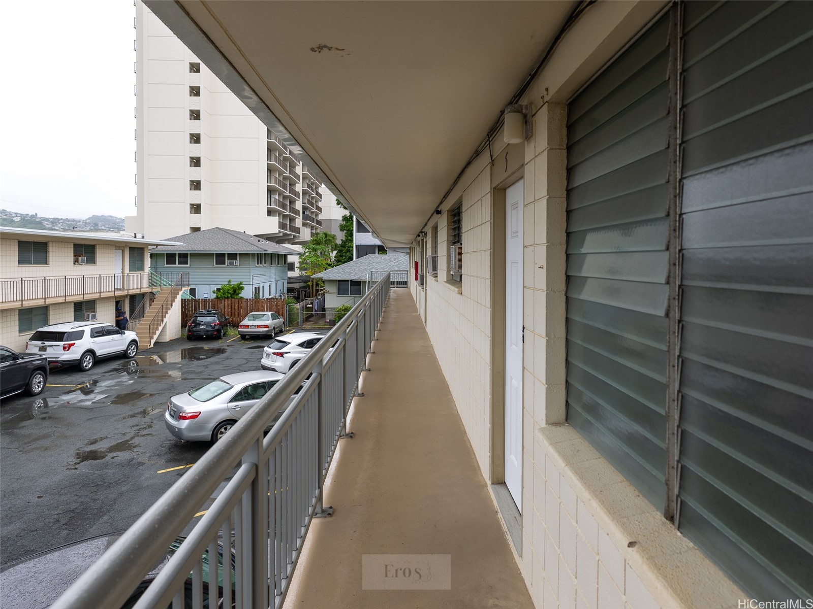 Apartment building walkway overlooking a parking lot, with exterior doors and a metal railing.