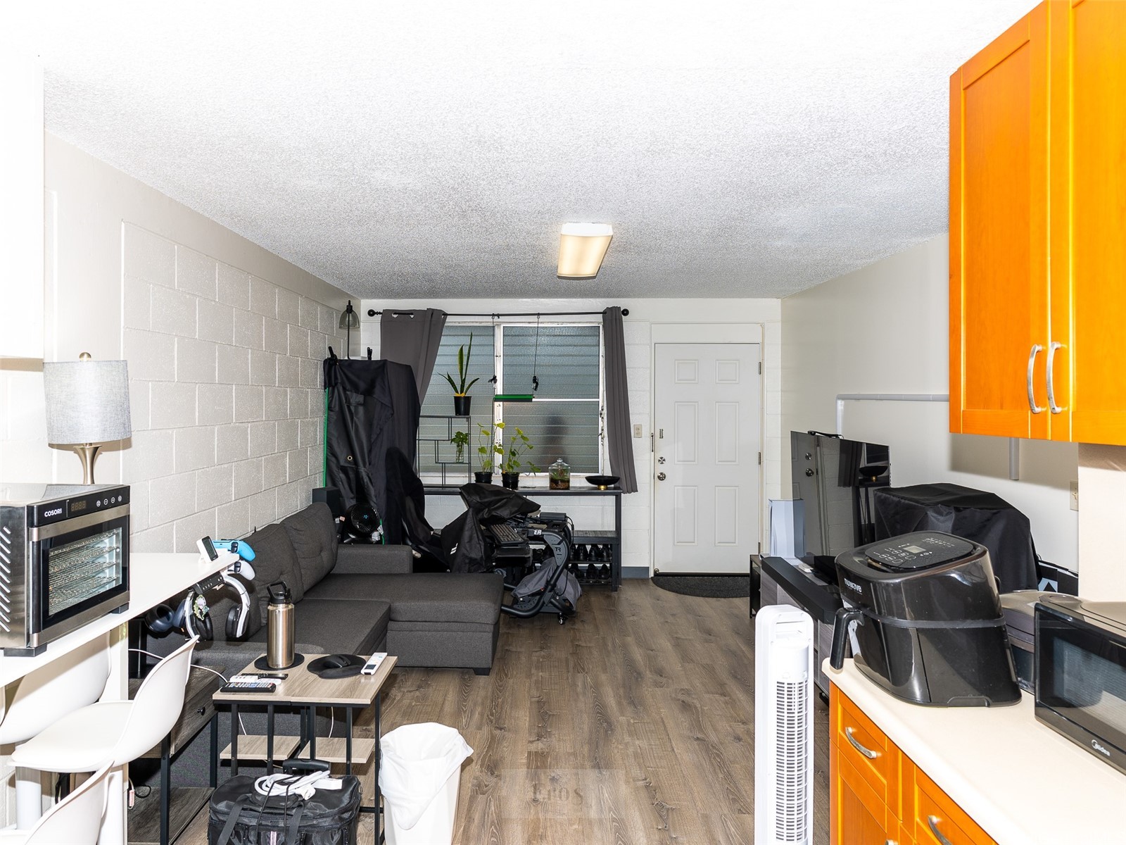 Furnished studio with gray sofa, wood-look floors, and bright orange kitchen cabinets.