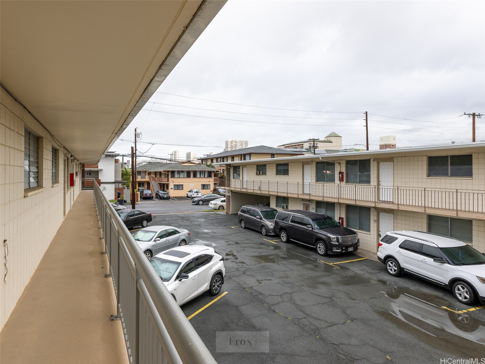 Apartment building and parking lot viewed from an upper-level walkway, with parked cars and exterior corridors.