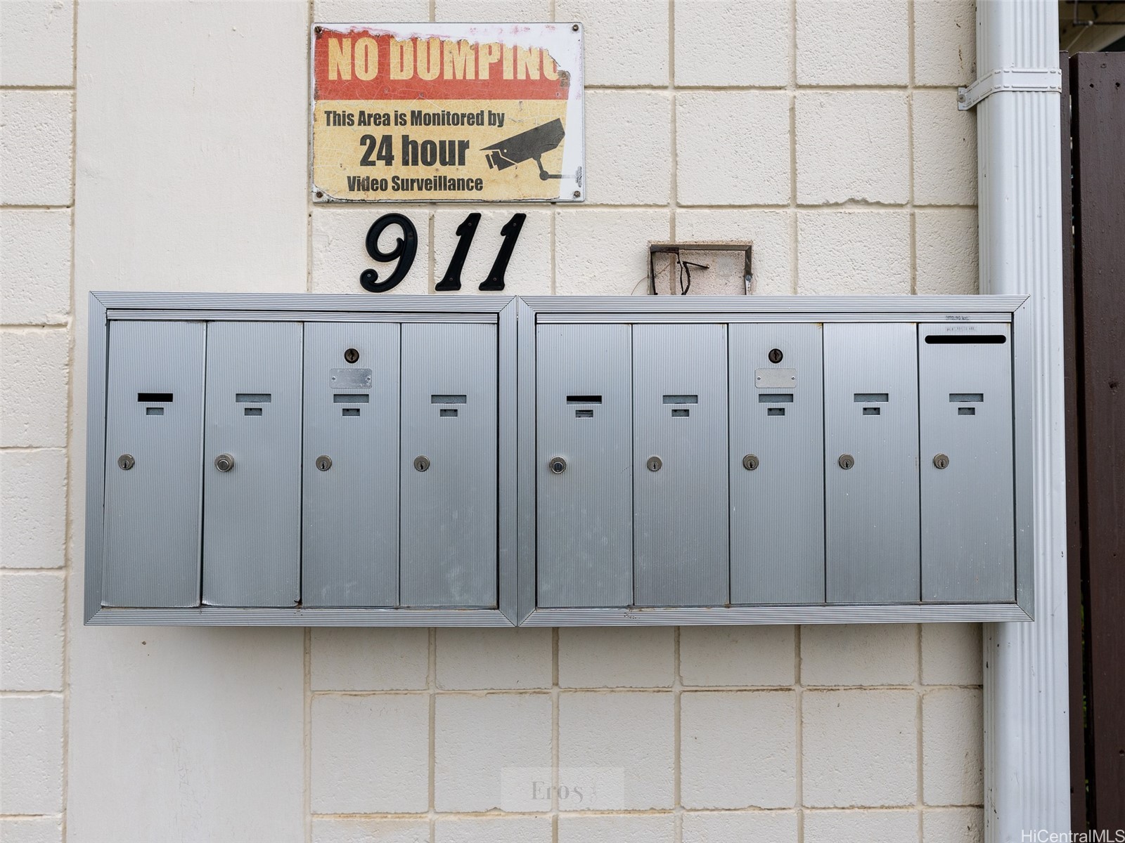 Metal mailboxes beneath a no-dumping and video surveillance sign, with the number 911 above.
