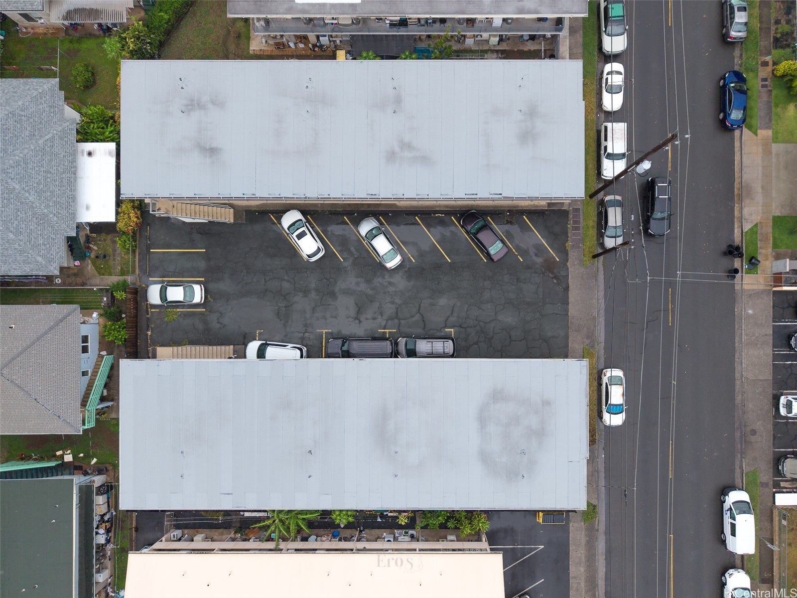 Aerial view of two commercial buildings and a parking lot with marked spaces and parked cars.