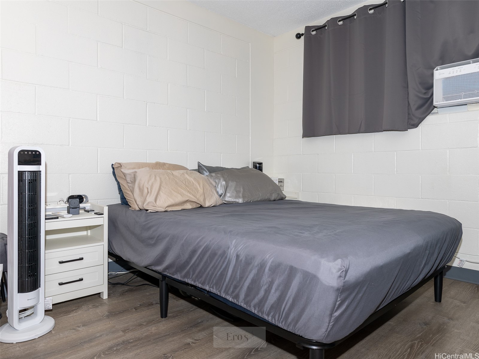 Bedroom with a gray-covered bed, white cinderblock walls, and a window air conditioner.