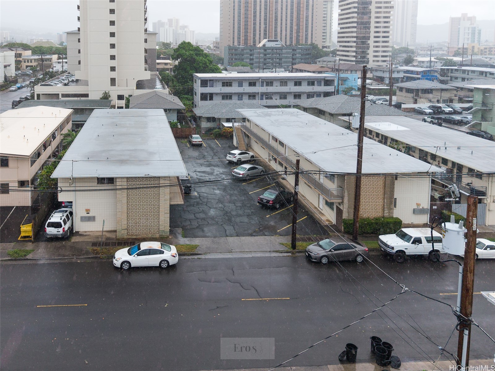 Low-rise Honolulu apartment buildings with a central parking area and high-rises behind them.