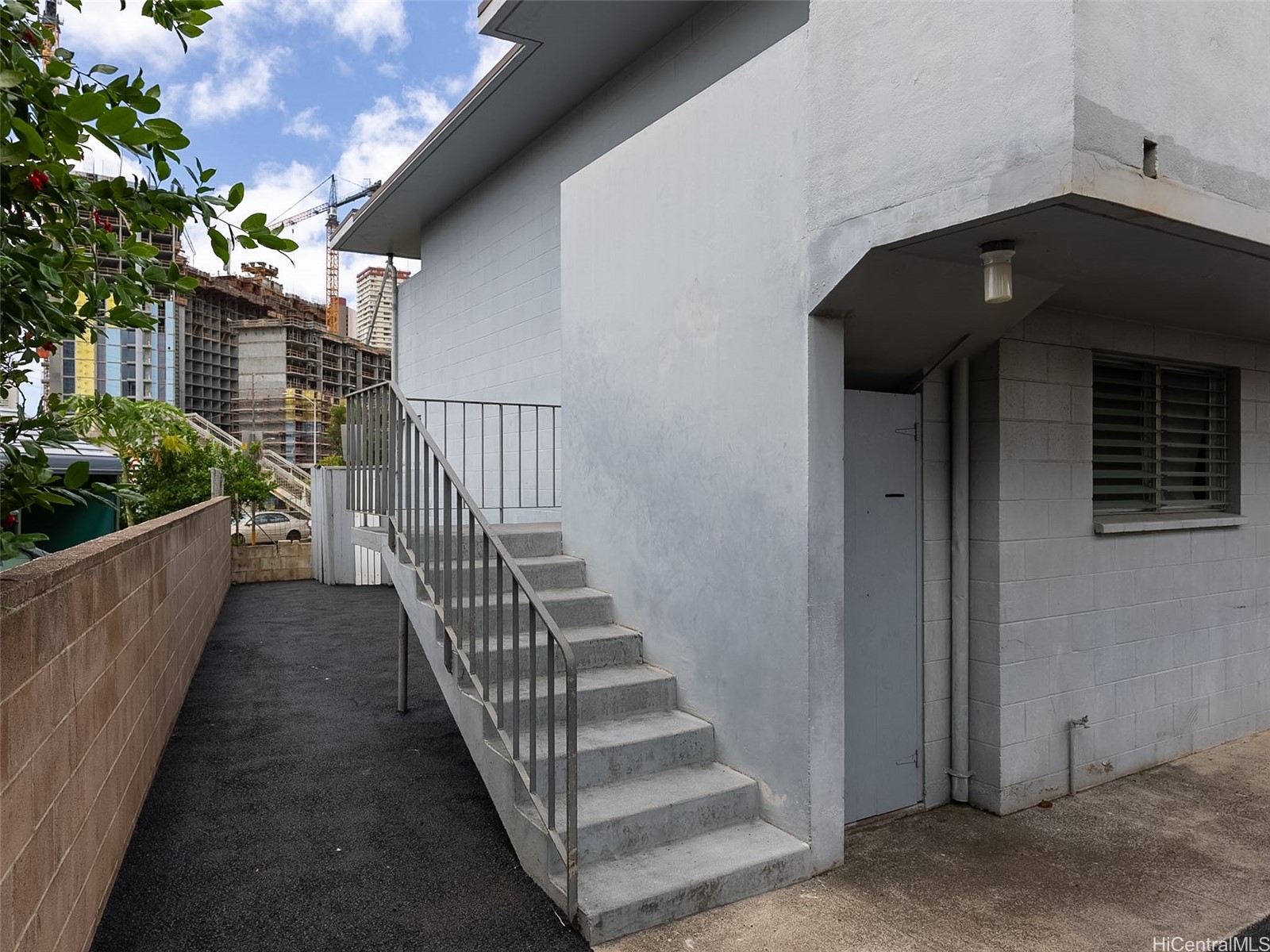 White building exterior with concrete entrance stairs, metal railings, and a paved side path.