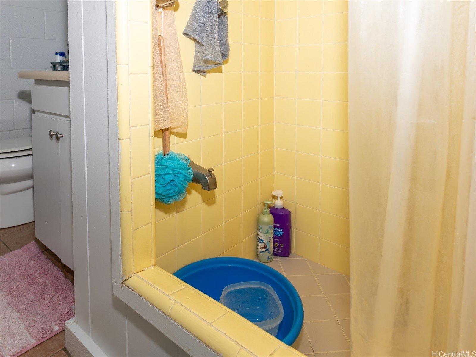 Yellow-tiled bathroom shower with a beige curtain and blue plastic basin.