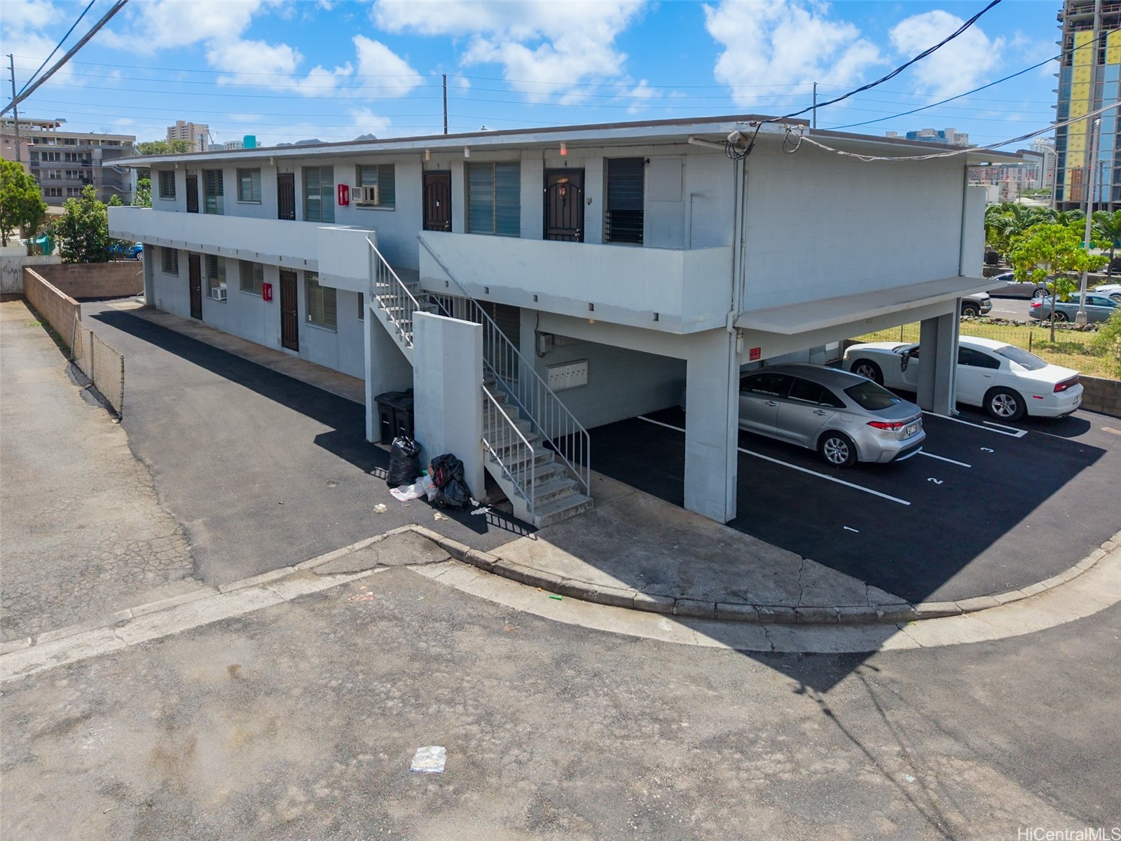 Two-story apartment building with exterior staircases and covered parking on a paved corner lot.