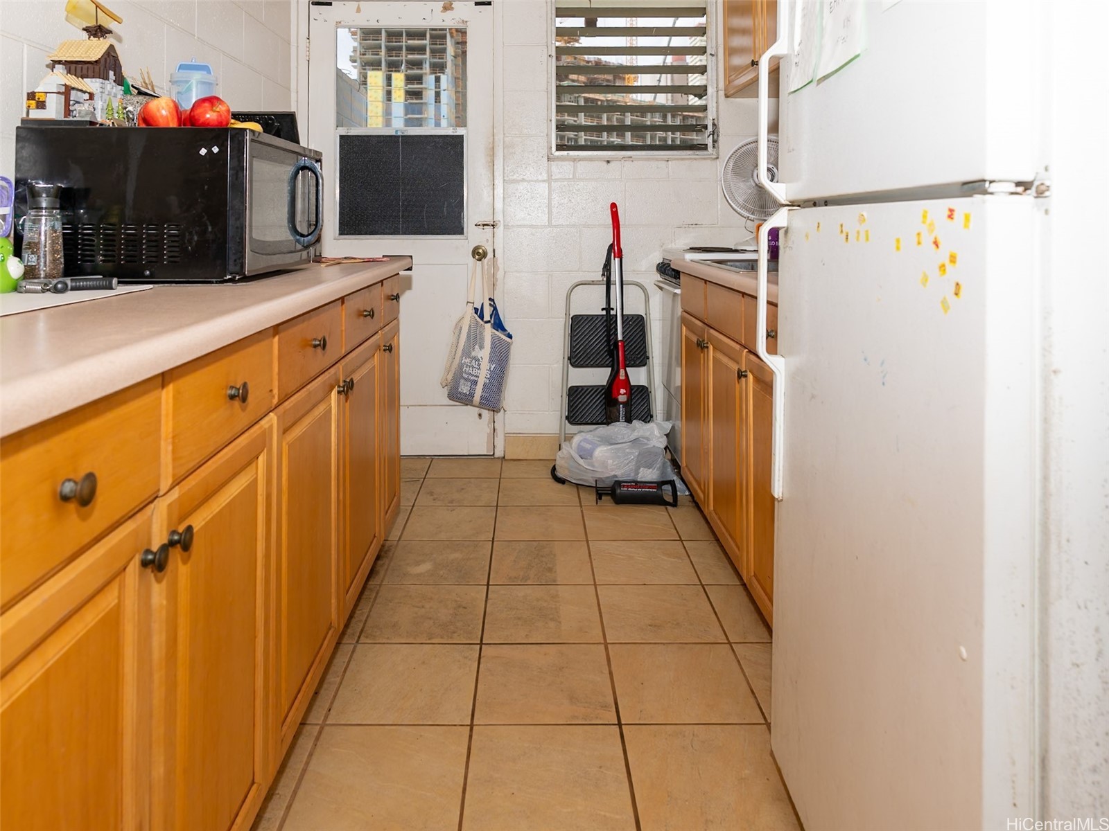 Narrow kitchen with wooden cabinets, tiled floor, and a large white refrigerator.