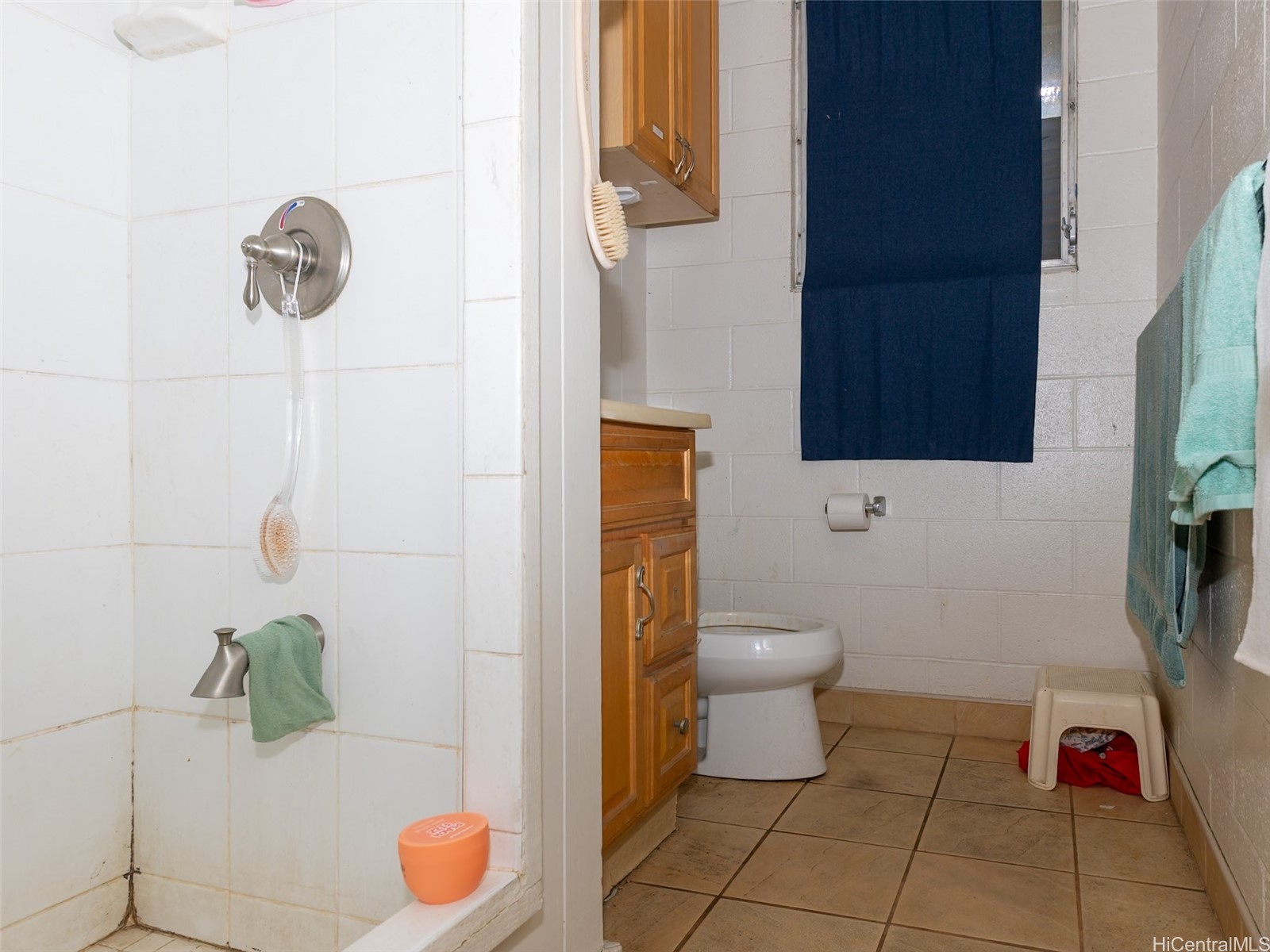 Bathroom with tiled shower, wooden vanity, toilet, and blue curtain.