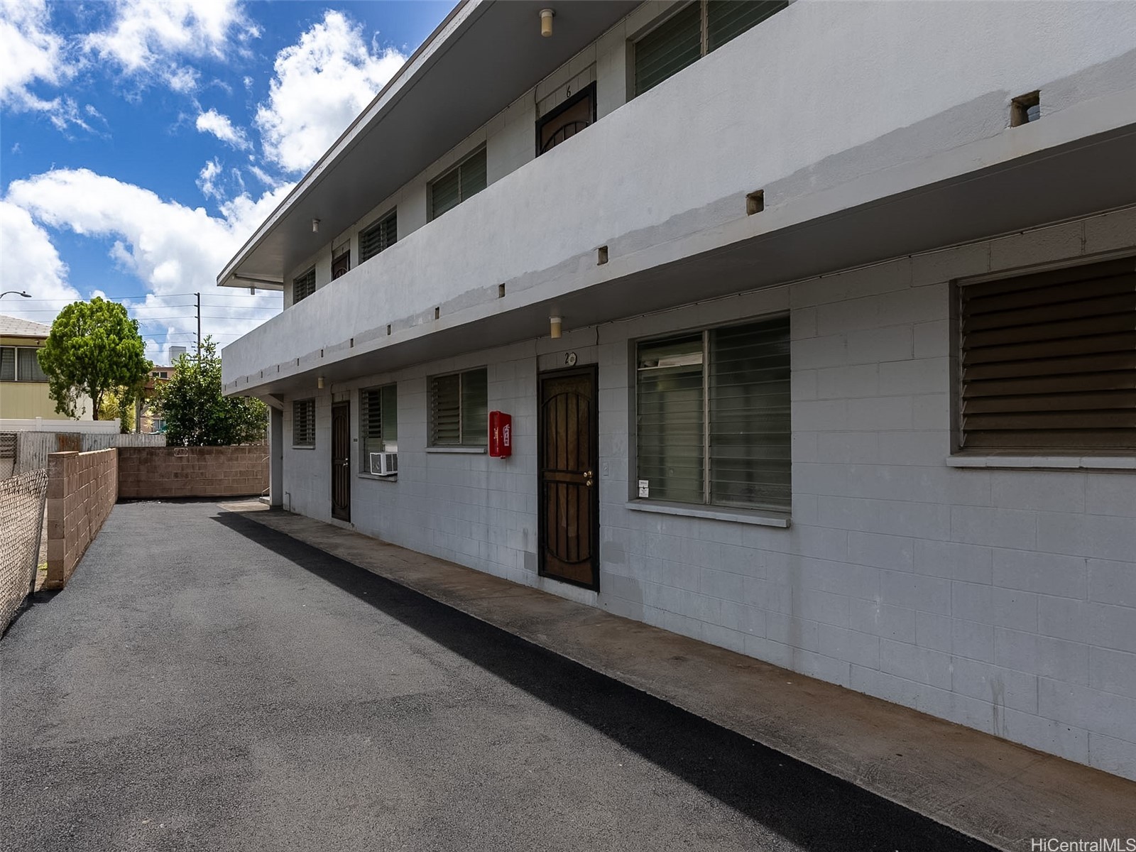 Two-story white apartment building with an upper balcony and asphalt driveway.