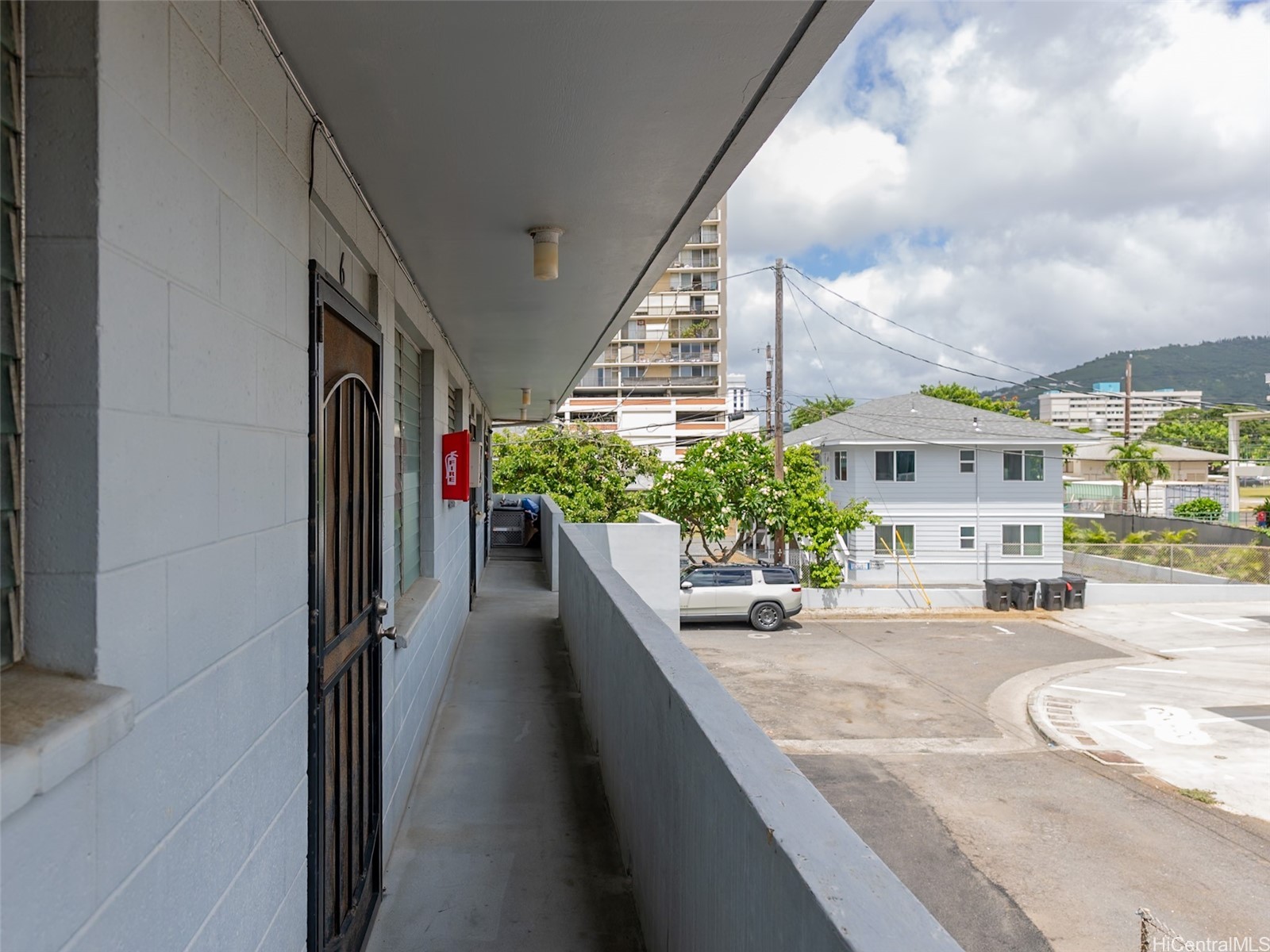 Covered exterior walkway beside the building, overlooking a parking area and green hillside.