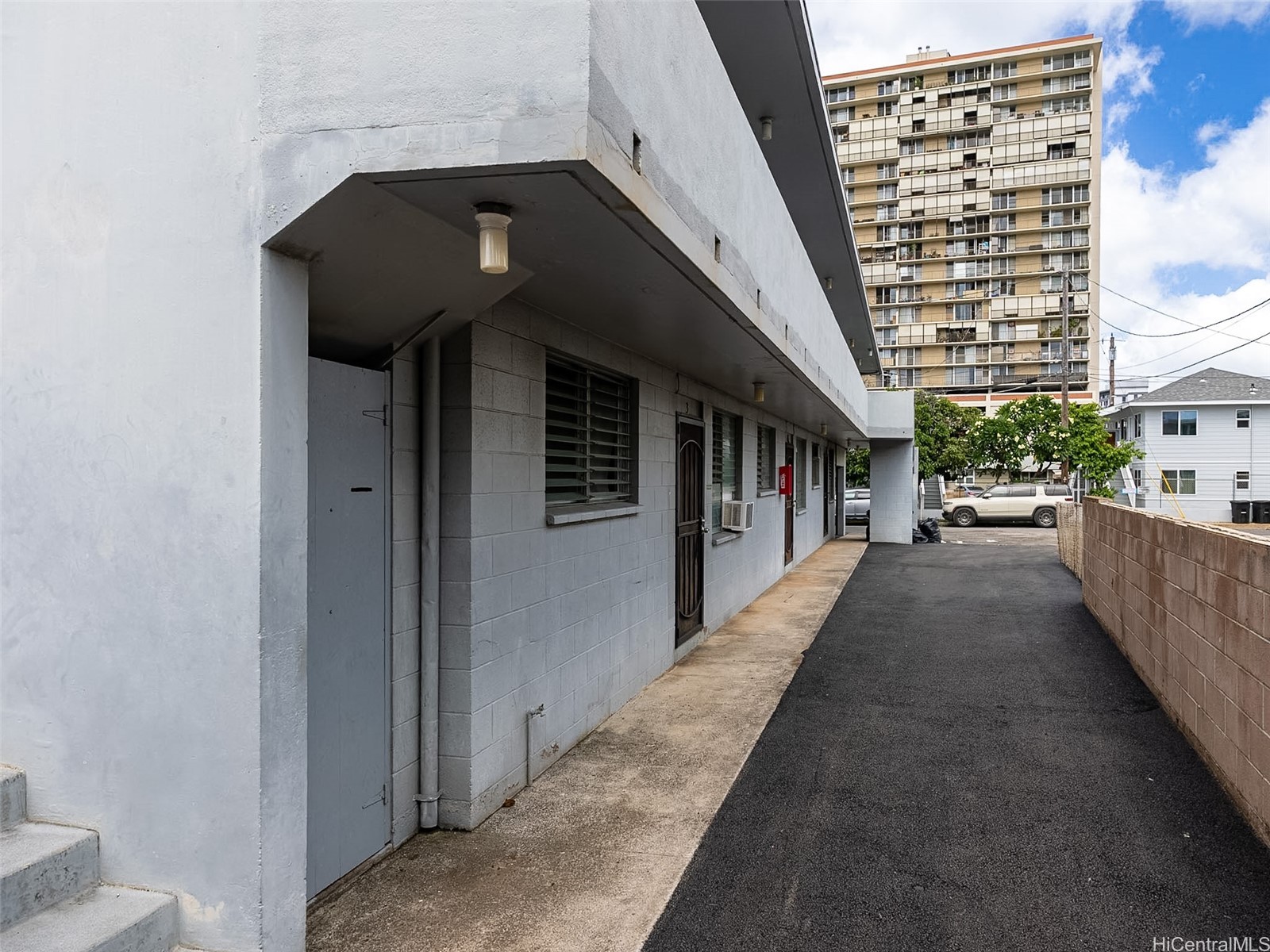 Low-rise building’s gray masonry side entrance beside a paved access lane.