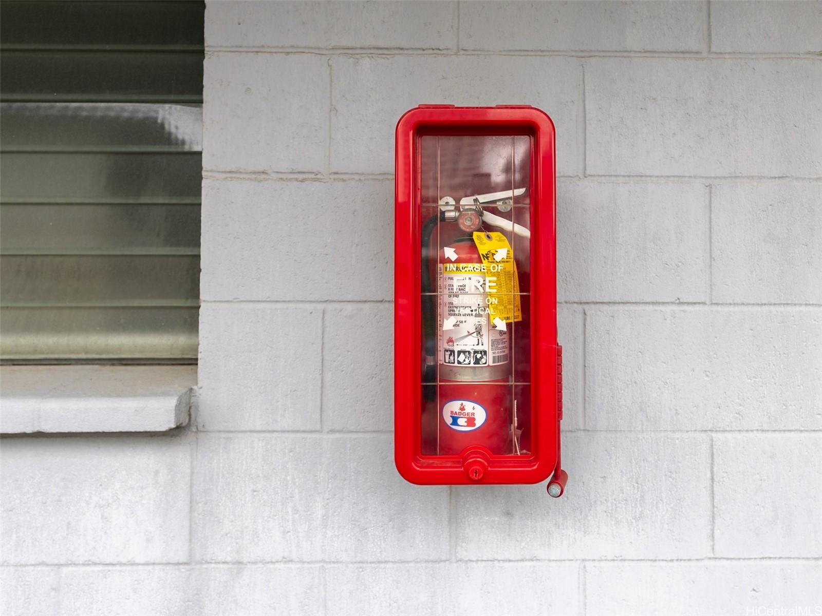 Red fire extinguisher in a wall-mounted cabinet beside a window.