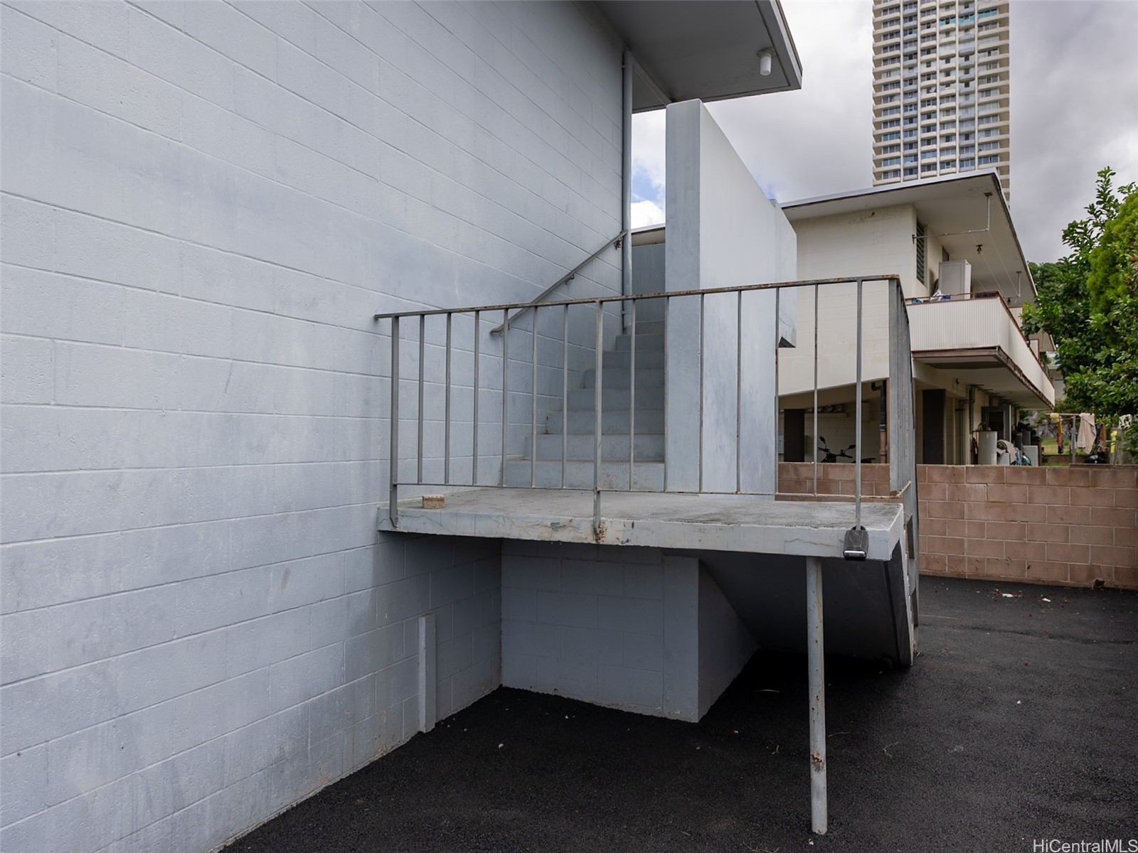 Light-gray building exterior with an elevated concrete landing, metal railings, and stairs.
