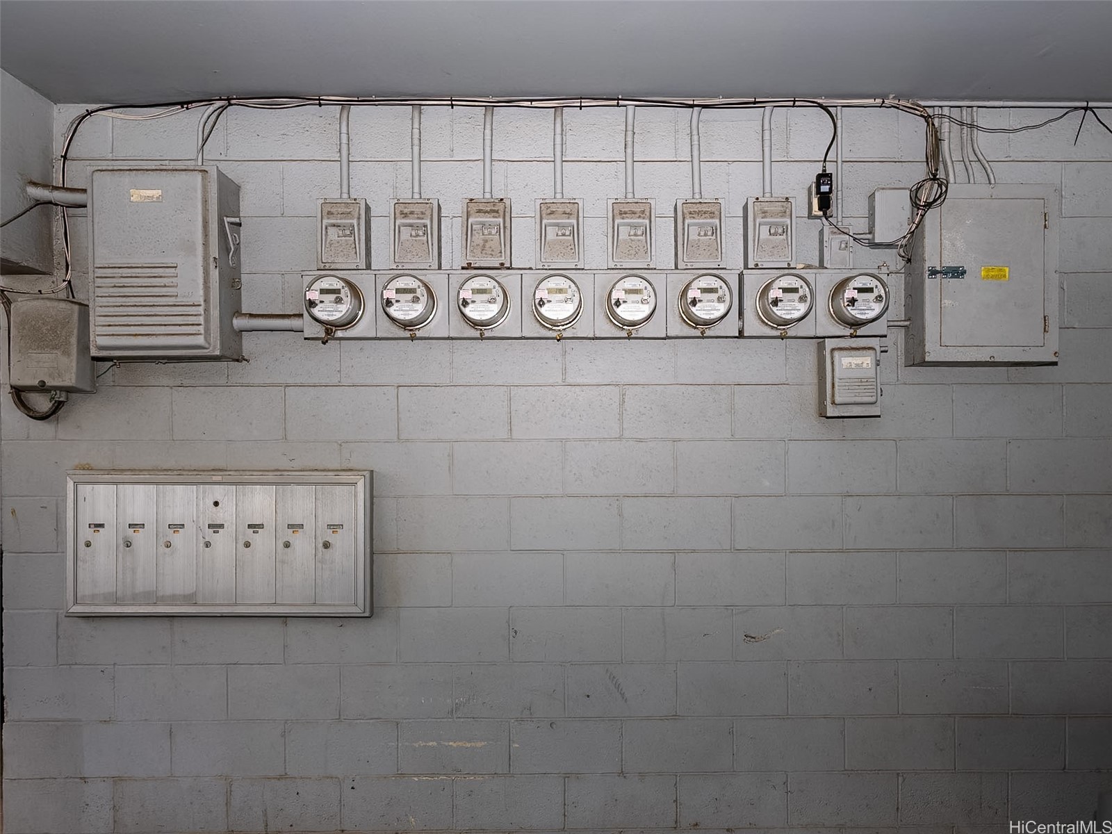 Utility area with eight electrical meters, breaker boxes, exposed wiring, and a row of mailboxes.