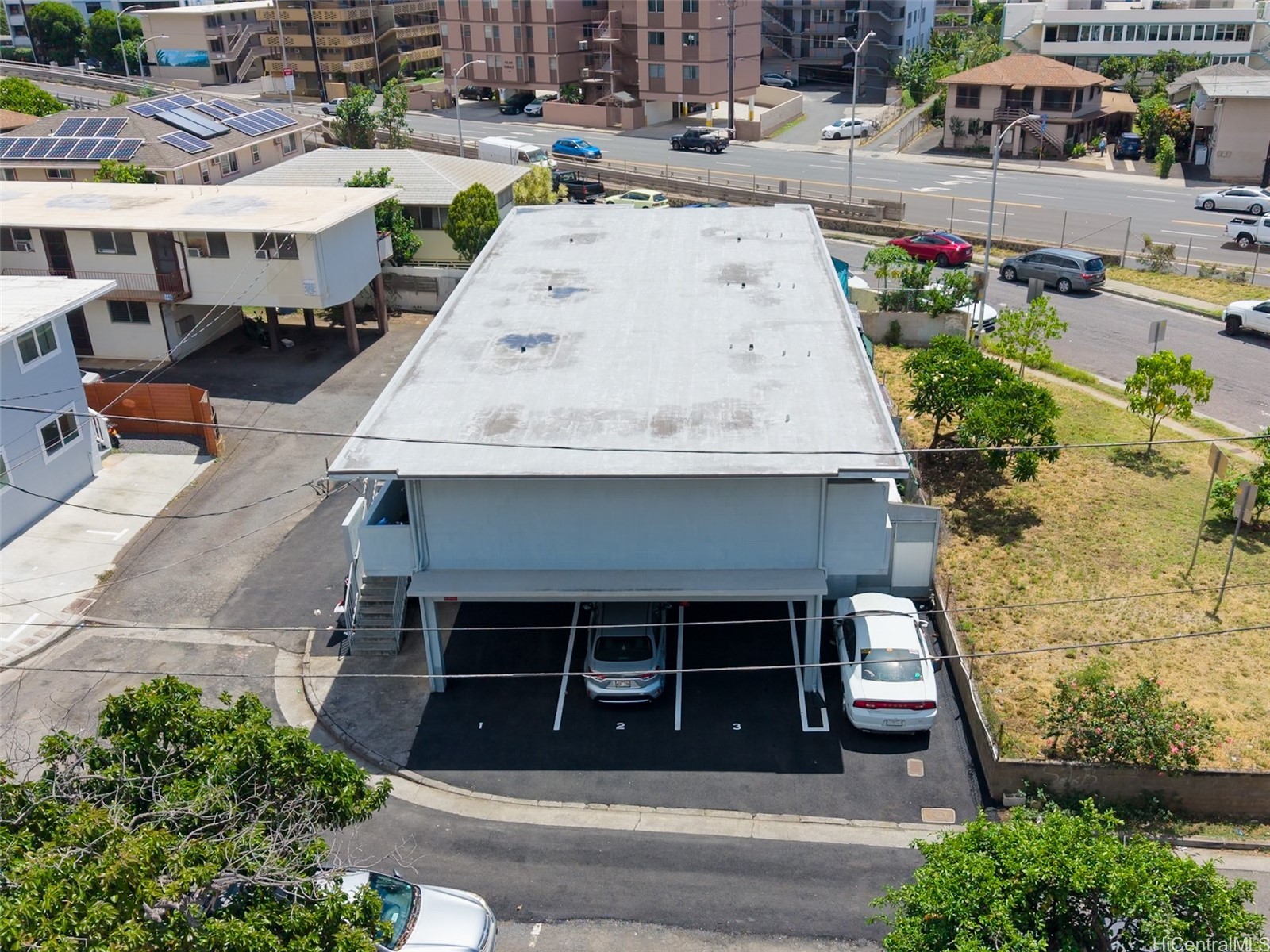 Aerial view of a flat-roofed commercial building with covered parking and marked spaces in Honolulu.