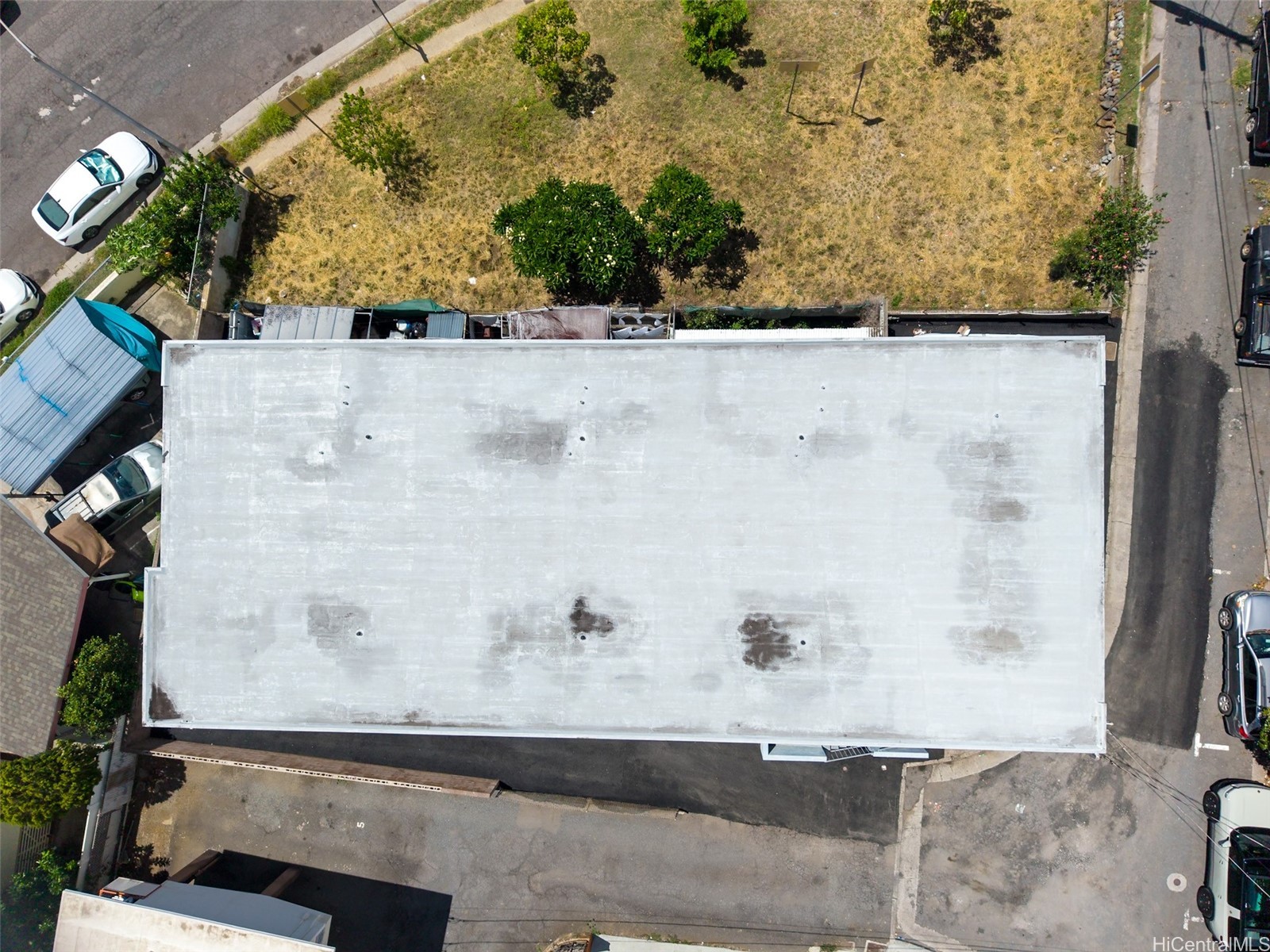 Aerial view of a large flat-roofed building beside a dry grassy lot and parking areas.