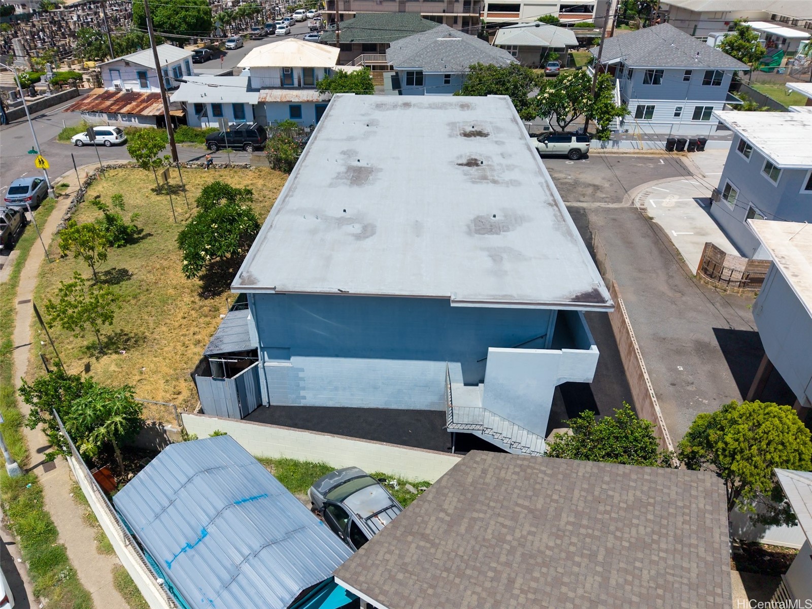 Blue commercial building with a broad flat roof, viewed from above among neighborhood homes.