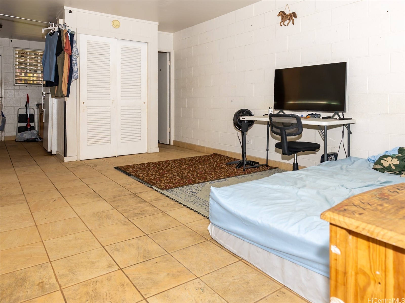 Compact bedroom with tiled floors, louvered closet doors, and a desk beneath a wall-mounted television.