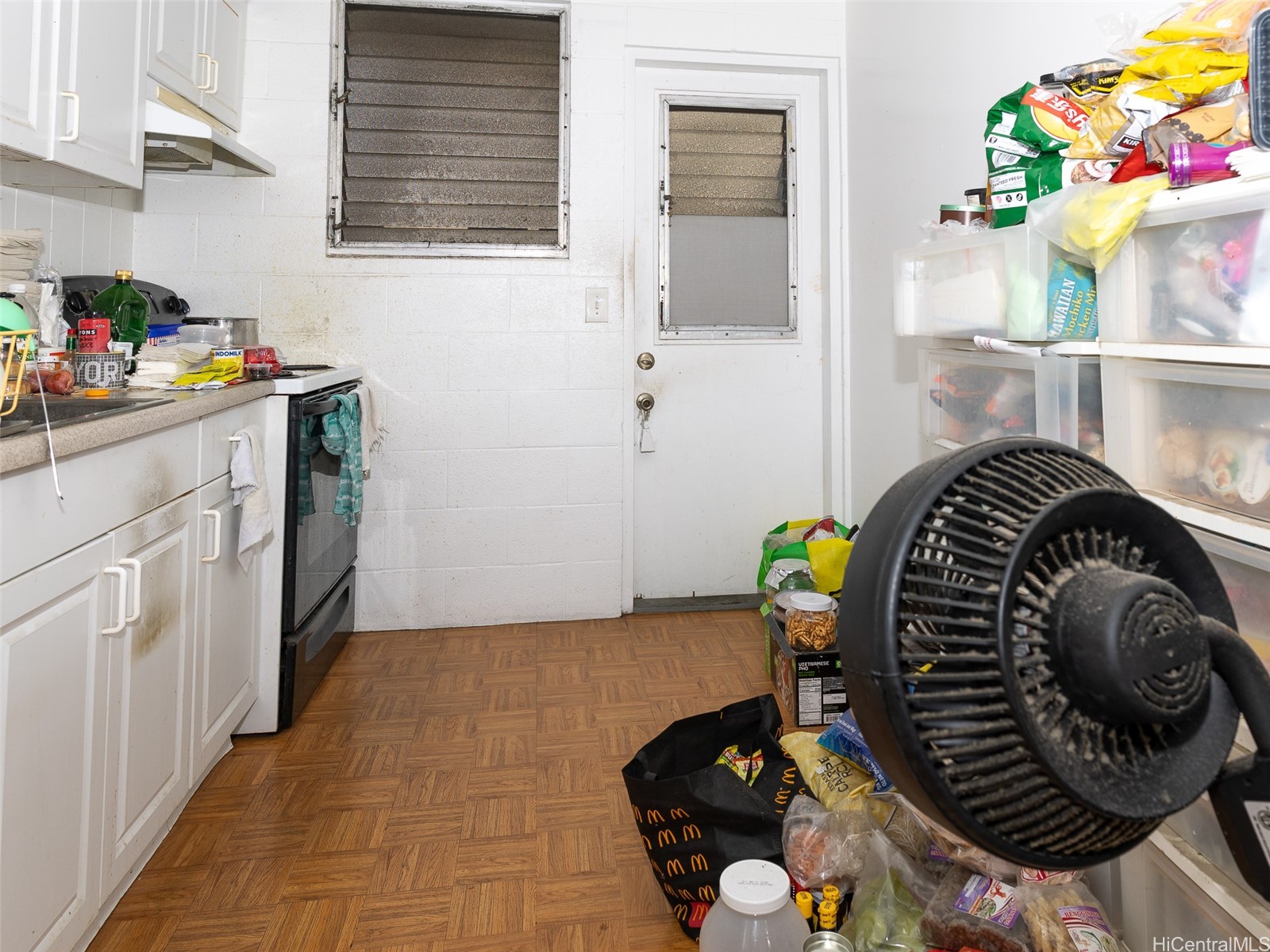 Cluttered kitchen with white cabinets, a stove, and food storage bins.