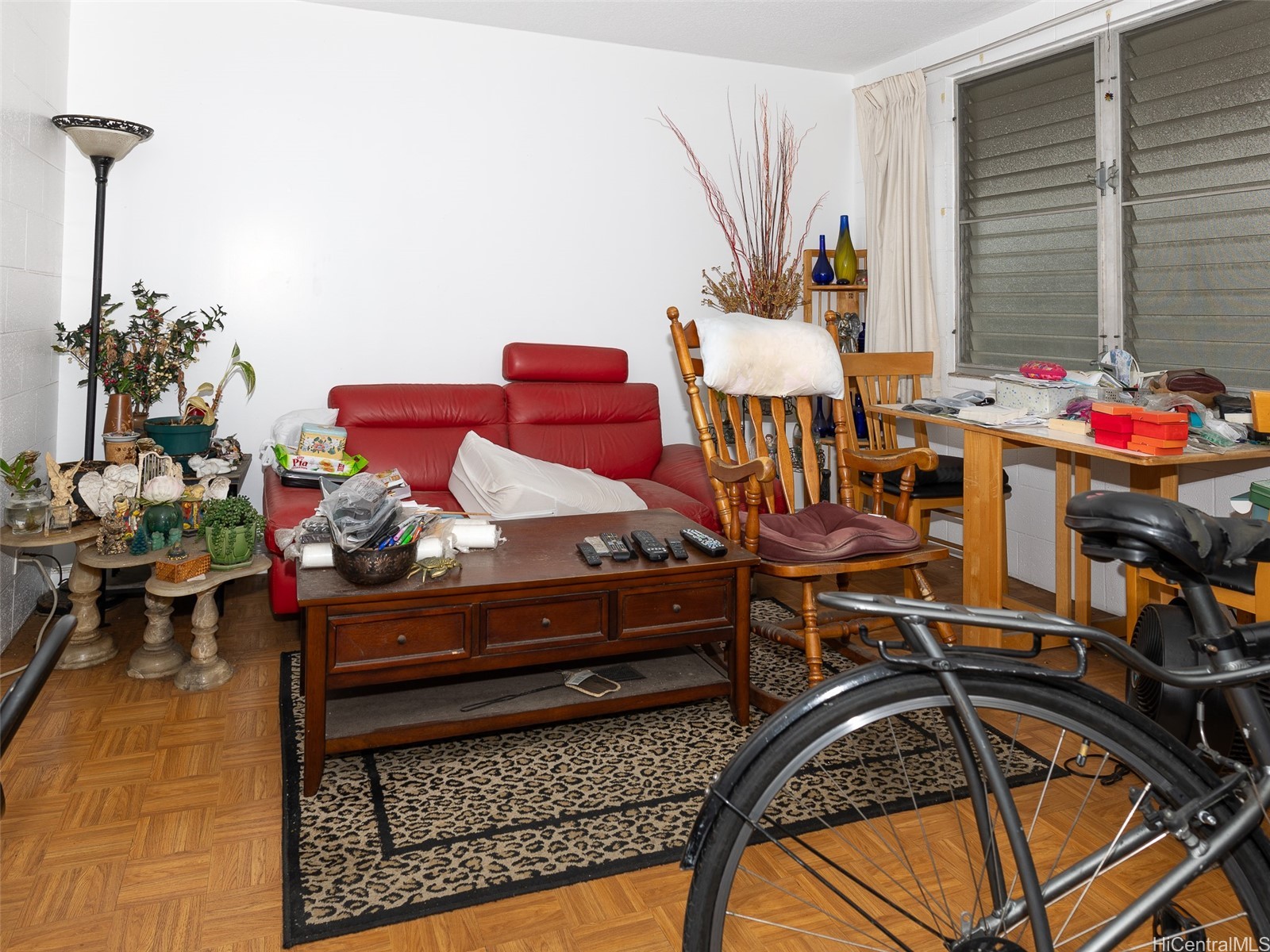Crowded living room with a red sofa, wooden furniture, and a bicycle in the foreground.