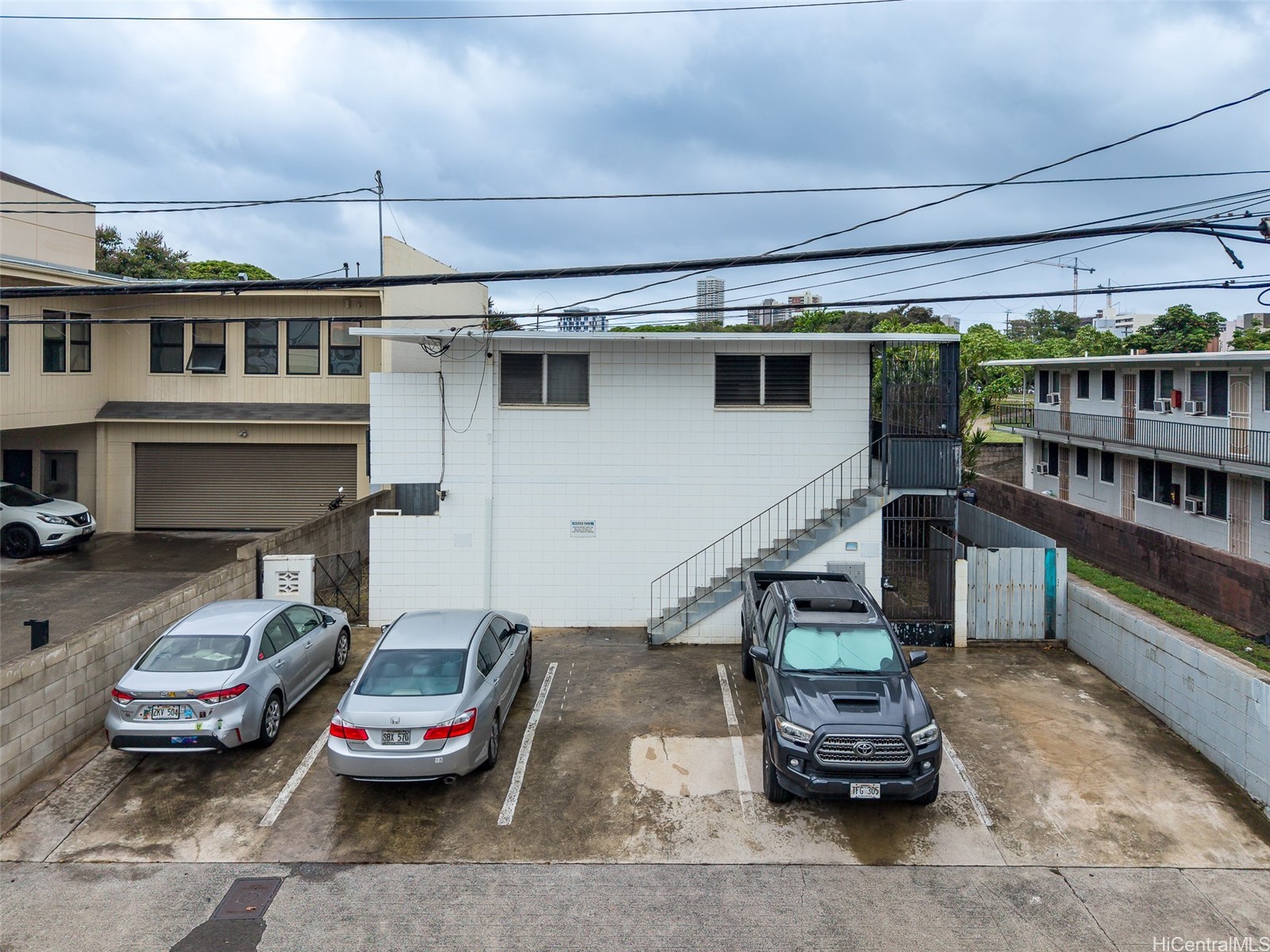 Property parking area with parked cars and an exterior staircase beside a white building.