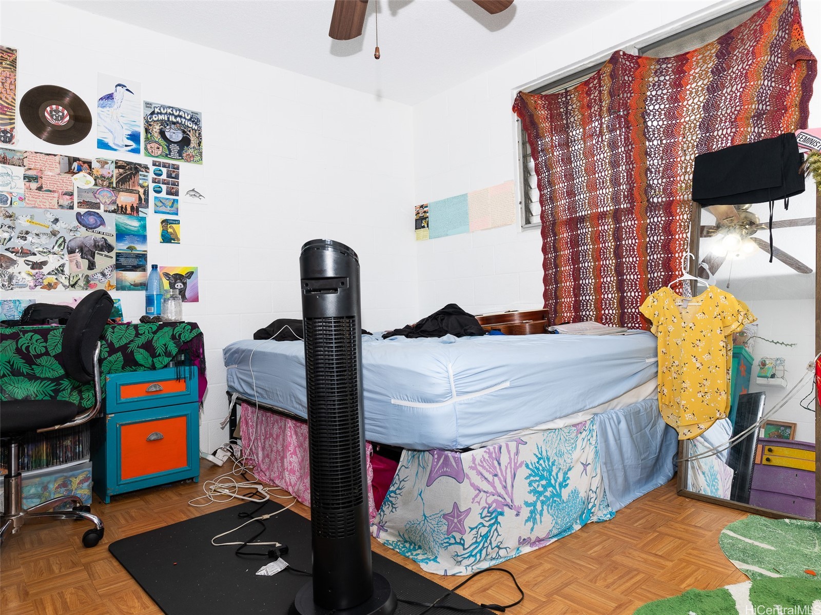 Bedroom with a raised bed, colorful patterned bedding, parquet floor, and a crocheted curtain over the window.