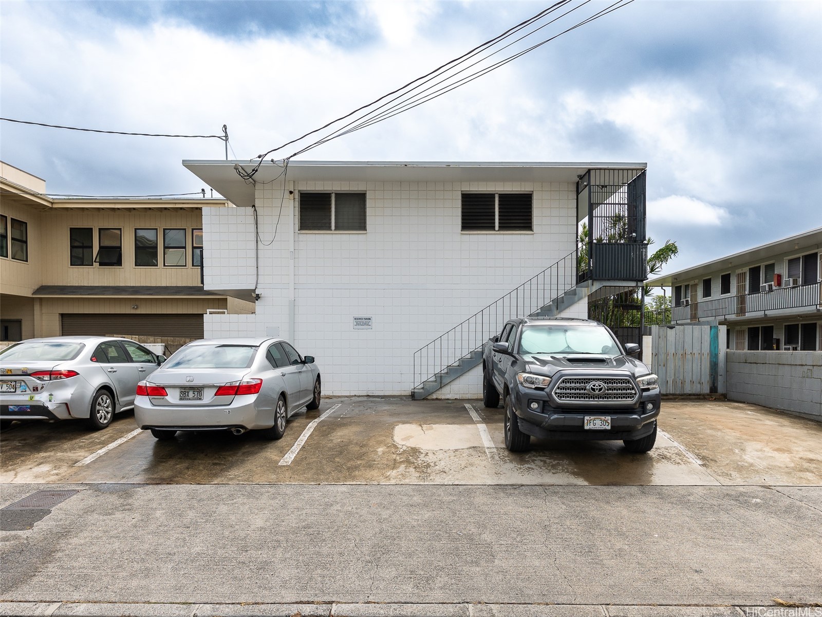 White two-story building with an exterior staircase and parking spaces in front.