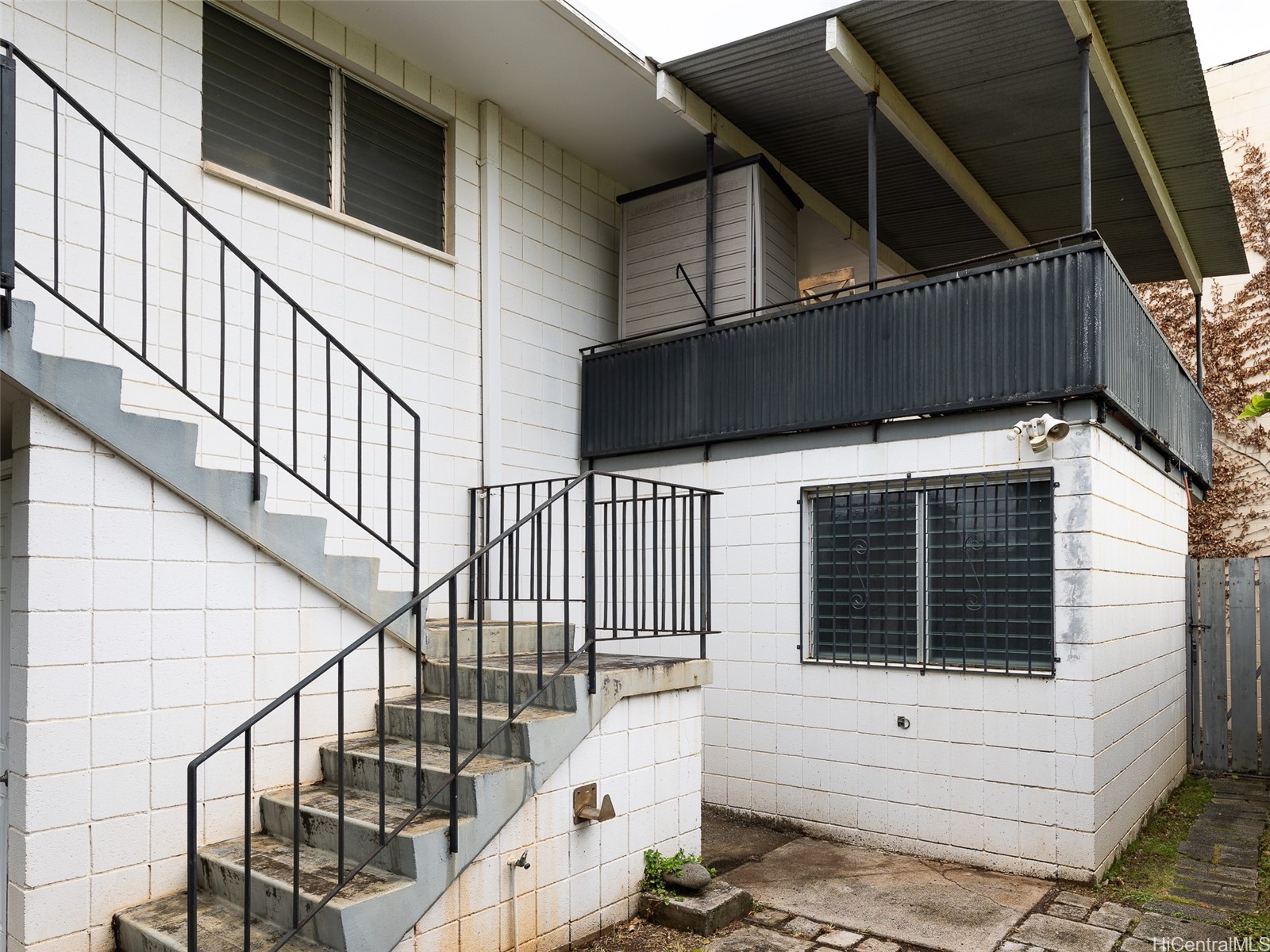 White block building exterior with an outdoor staircase, elevated balcony, and barred windows.
