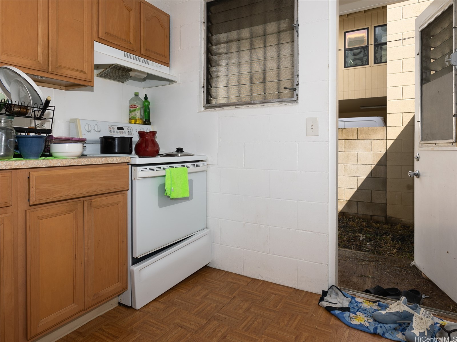Compact kitchen with wood cabinets and a white range, viewed beside an open door to the yard.