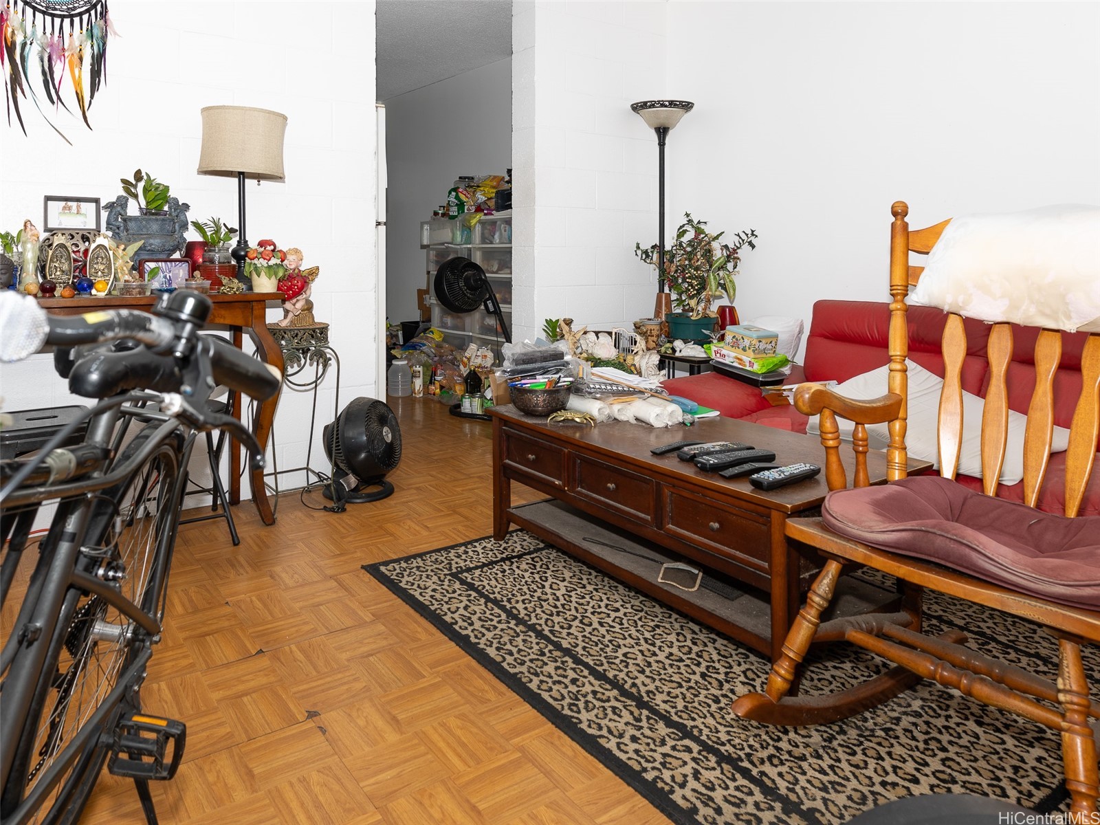 Cluttered living room with a red sofa, wooden coffee table, bicycle, and parquet flooring.