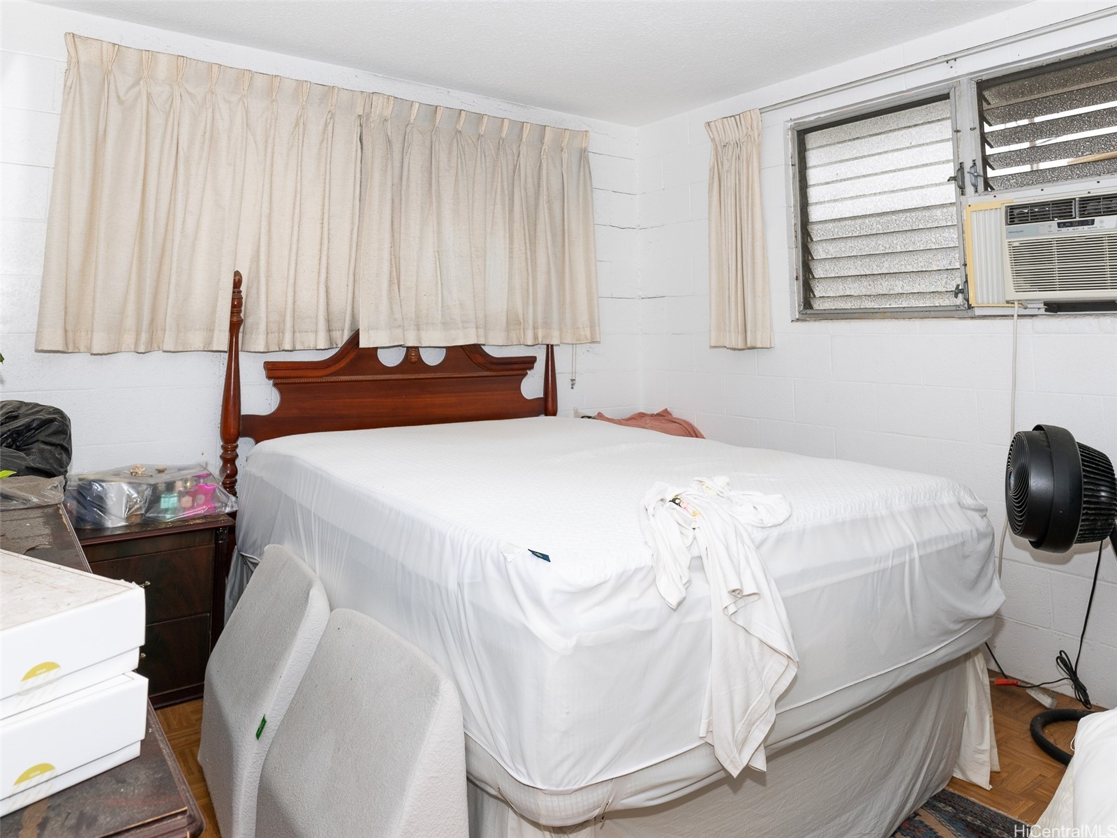 Bedroom with a large bed, carved dark wood headboard, and louvered window air conditioner.