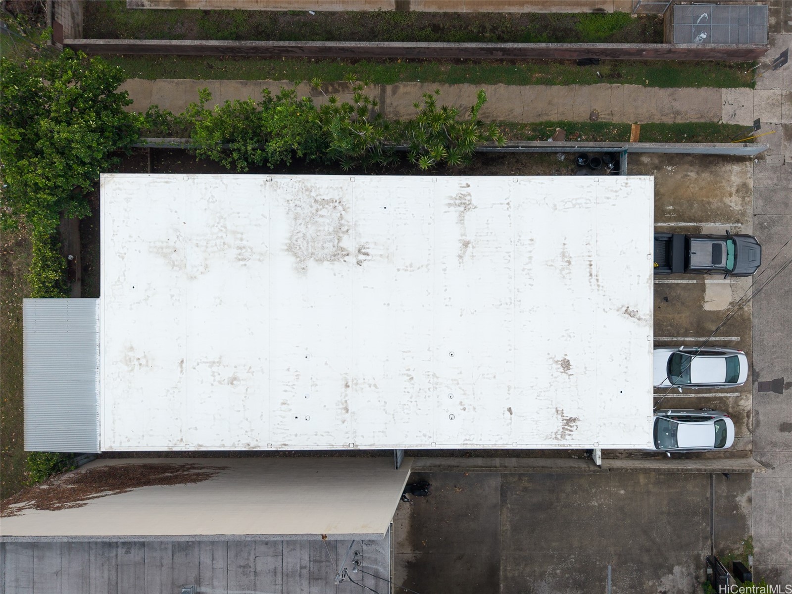 Aerial view of a commercial building with a large white roof and cars parked alongside.
