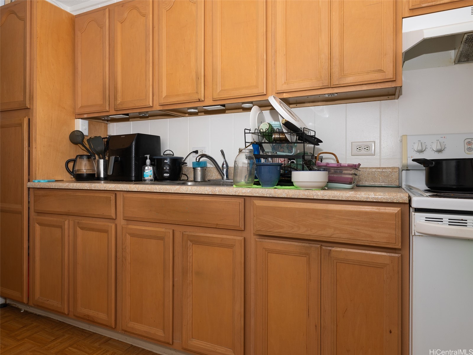 Kitchen with honey-colored cabinets, a crowded countertop, and a white electric range.