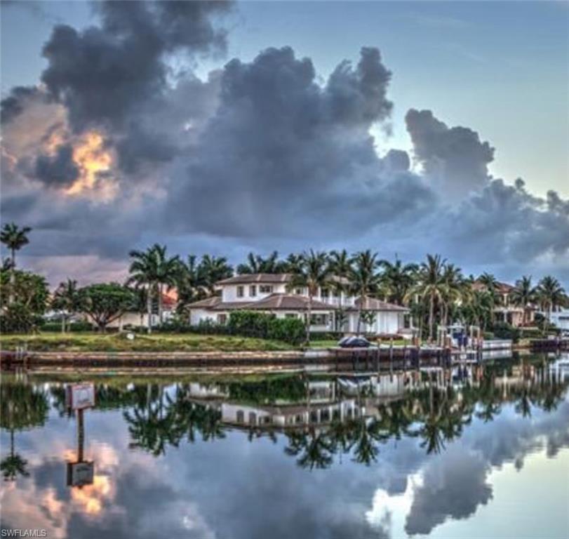 Waterfront home along a palm-lined canal at dusk, reflected in calm water.