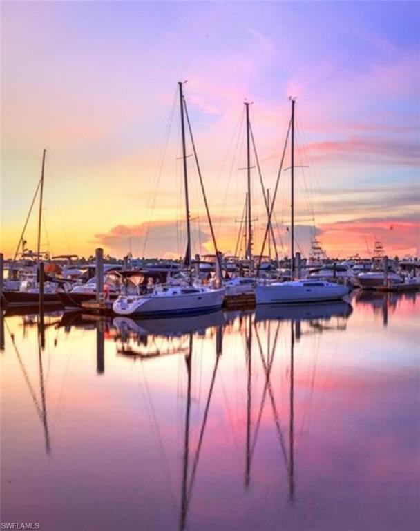 Marina with sailboats reflected in calm water beneath a colorful sunset sky.