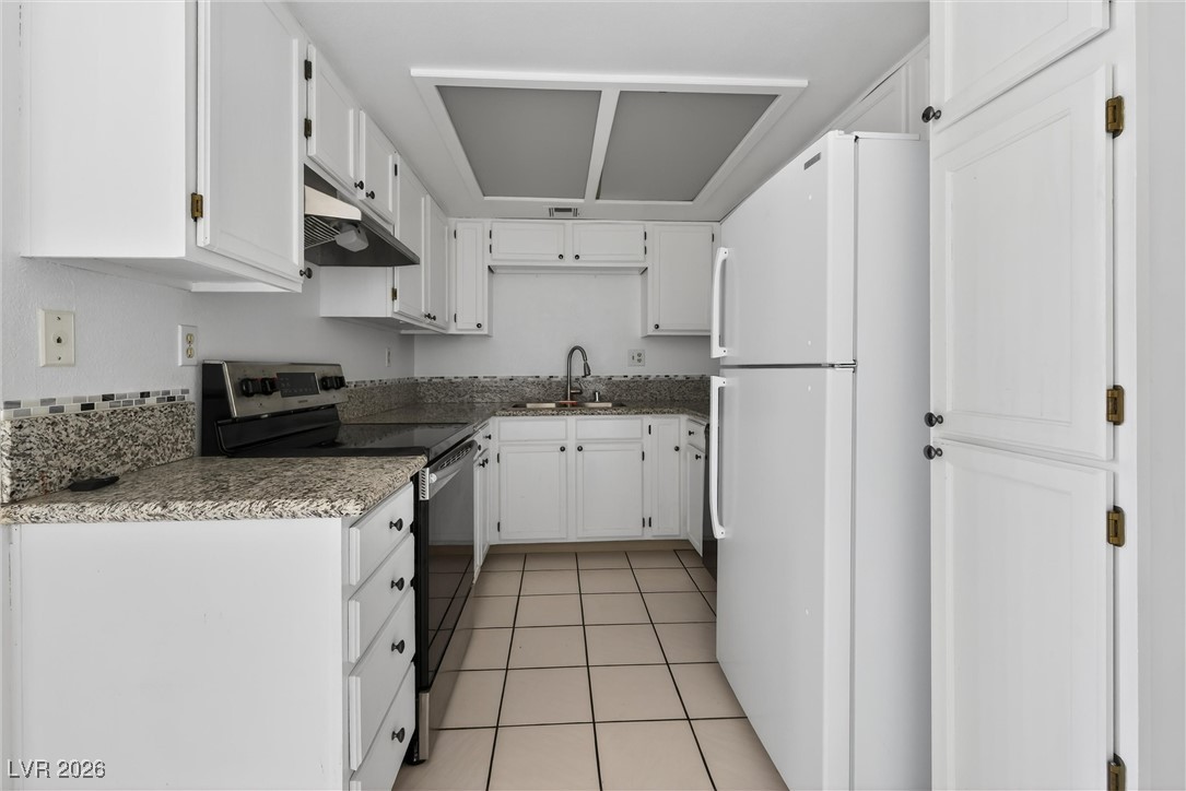 Kitchen with white cabinets, speckled granite counters, black range, and tiled floor.