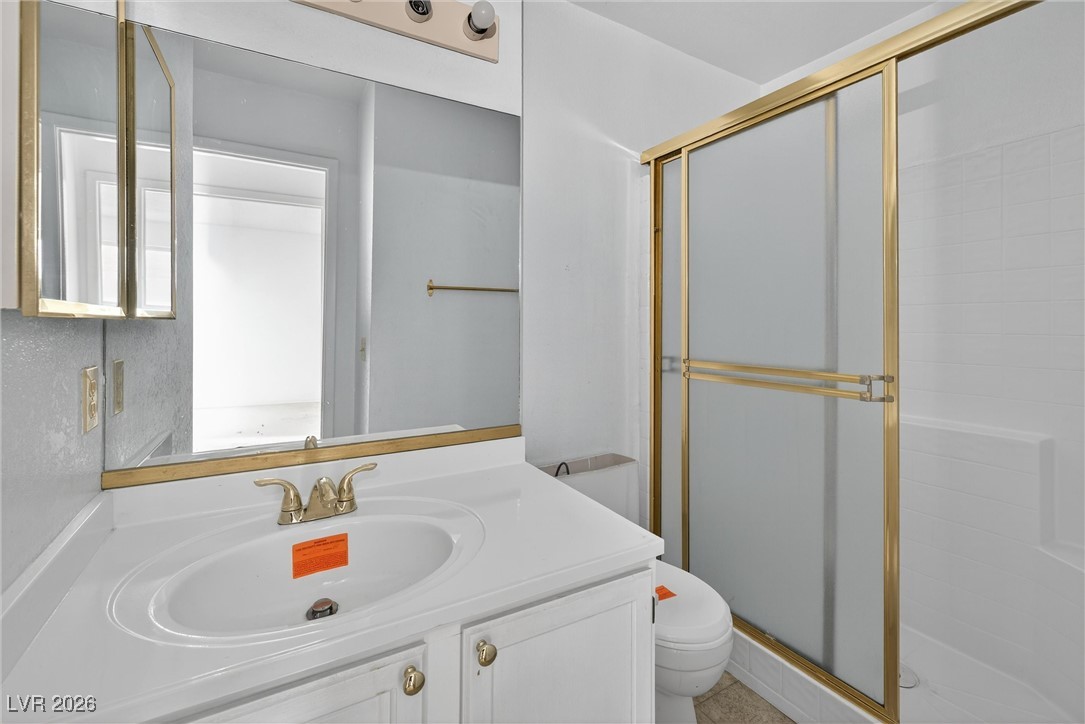 Bathroom with a white vanity, mirrored cabinet, and tub behind gold-framed frosted shower doors.