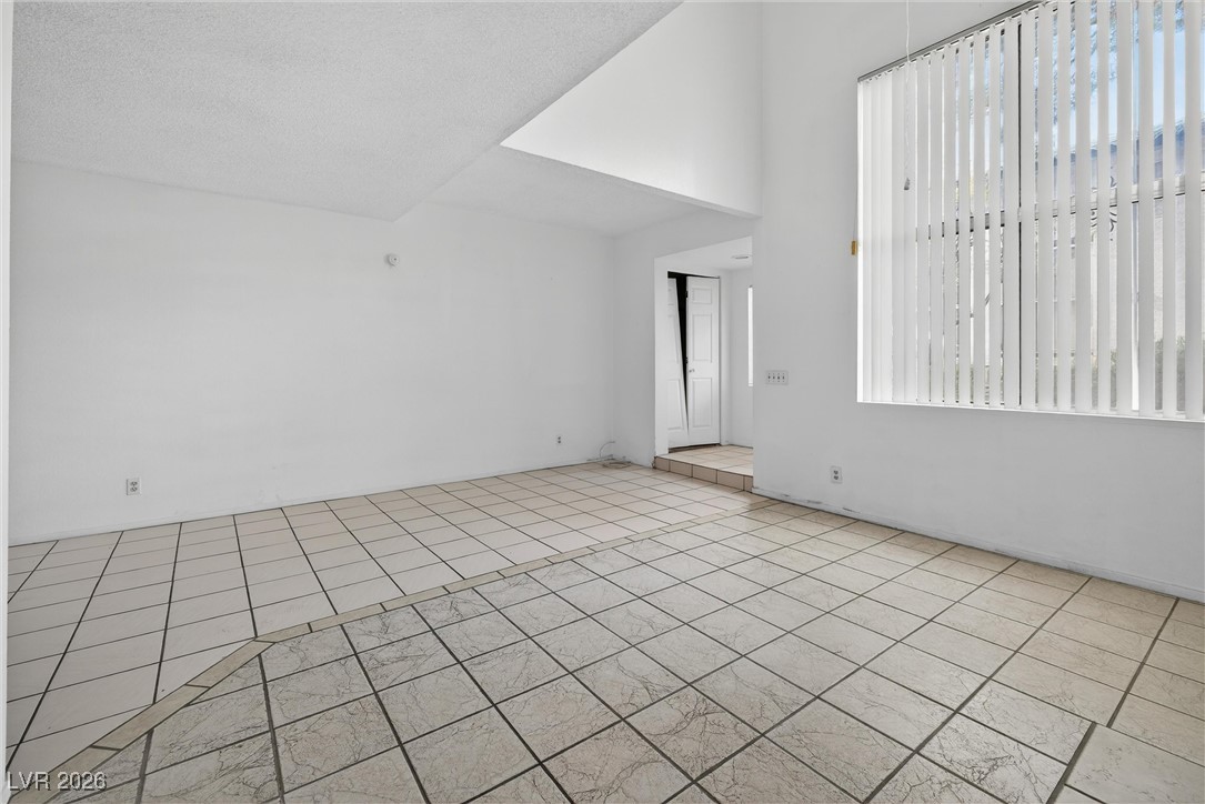 Empty room with tiled floors, a darker tile border, and a large window with vertical blinds.