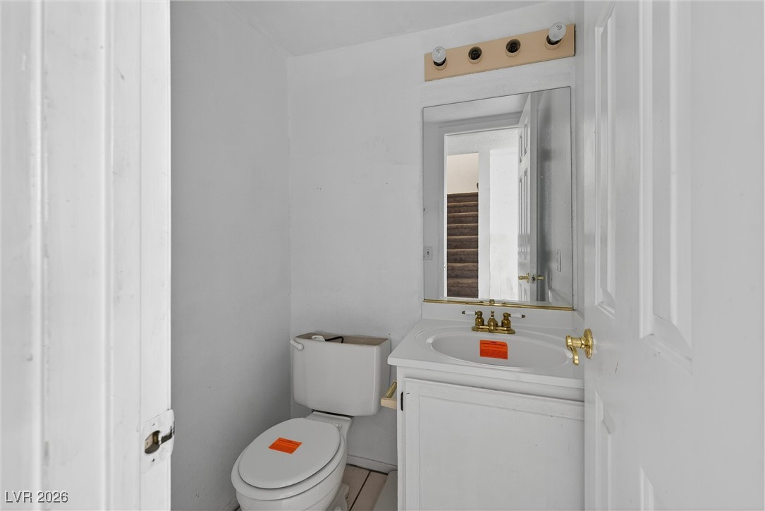 Small white bathroom with a toilet, vanity sink, brass-colored faucets, and a mirror reflecting stairs.