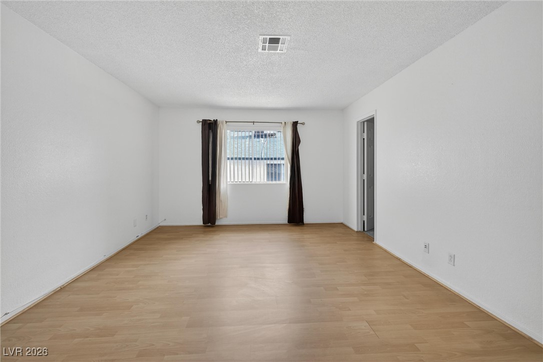 Vacant living room with light wood-look flooring, a curtained window, and a doorway.