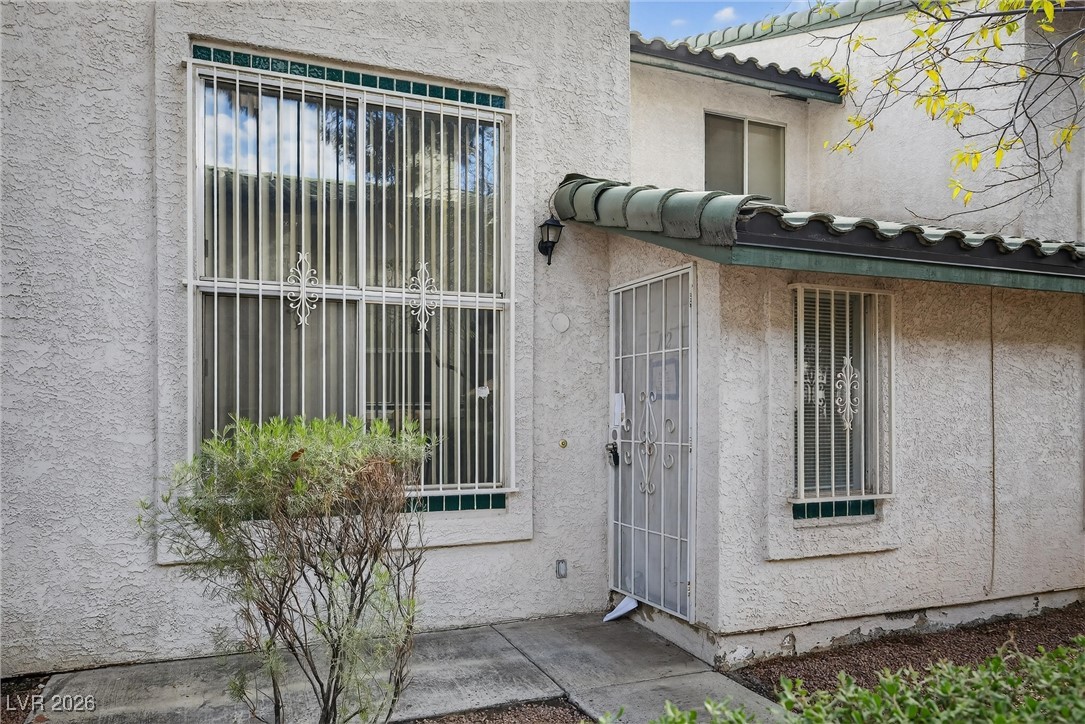 Stucco home exterior with barred windows, a security door, and a curved tile awning.